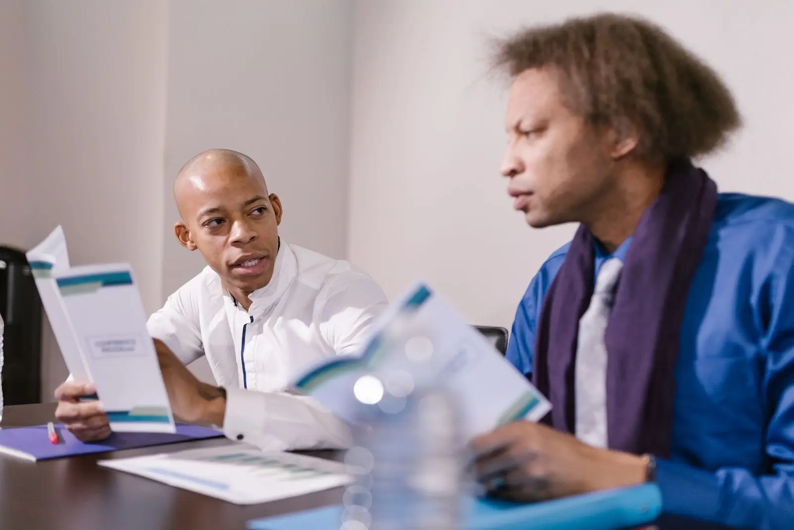 Two colleagues talk over printed leaflets at a meeting table.