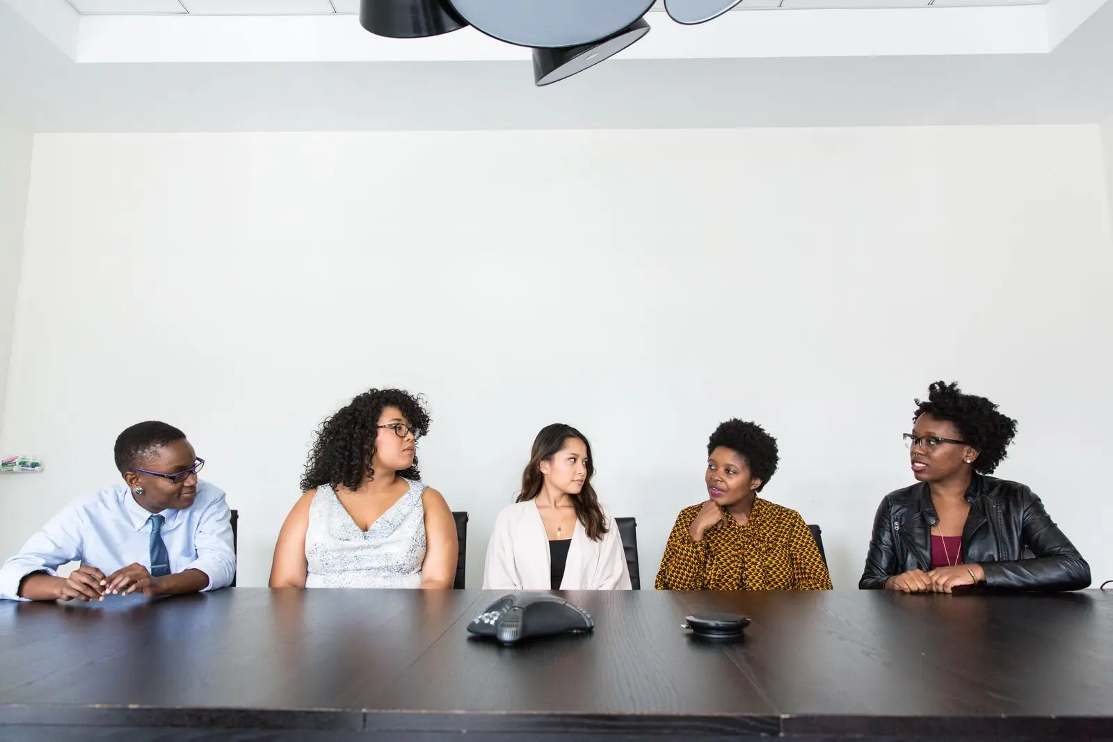 Five professionals sit side by side at a long table during a discussion.
