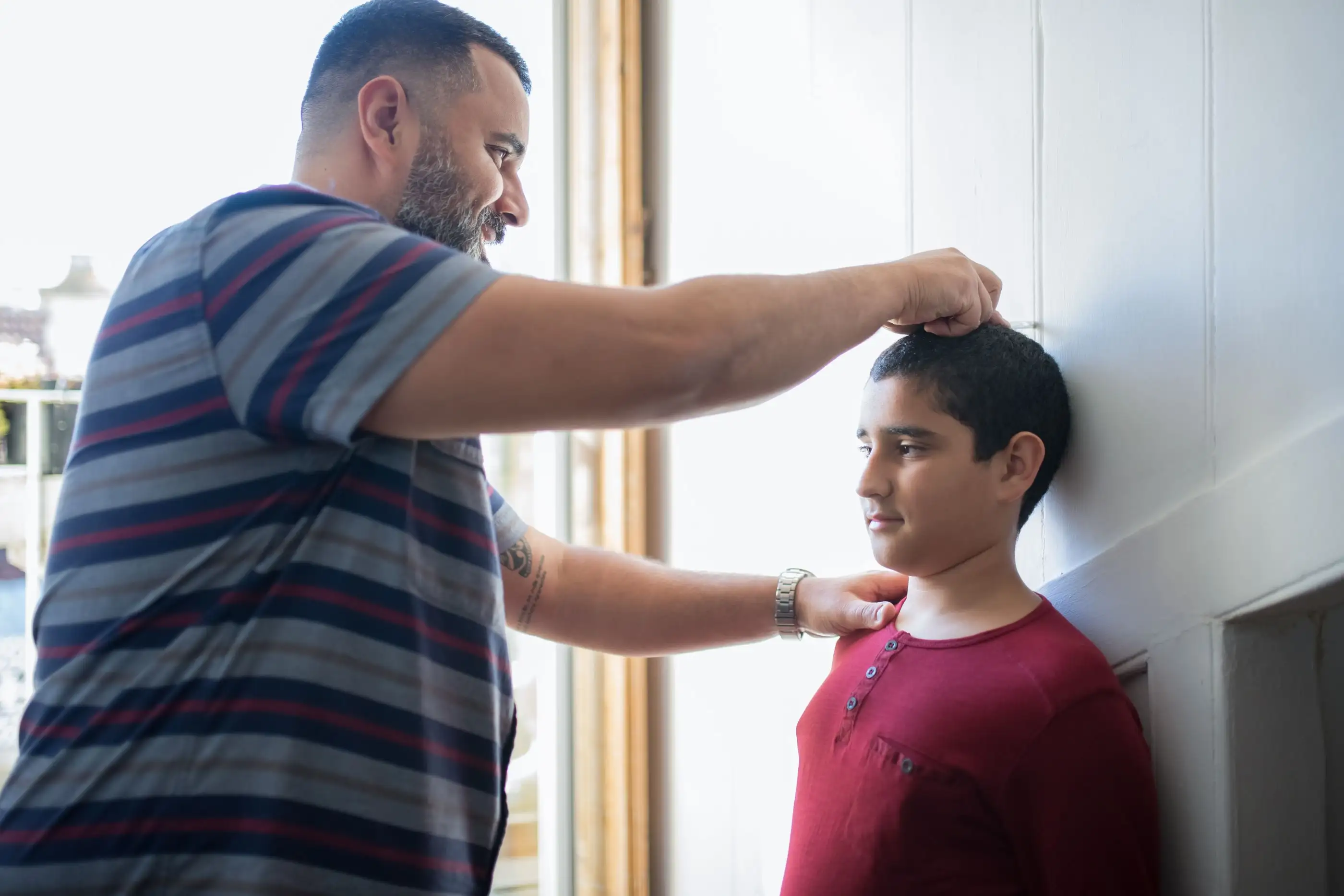 A father measures his son's height against a wall.