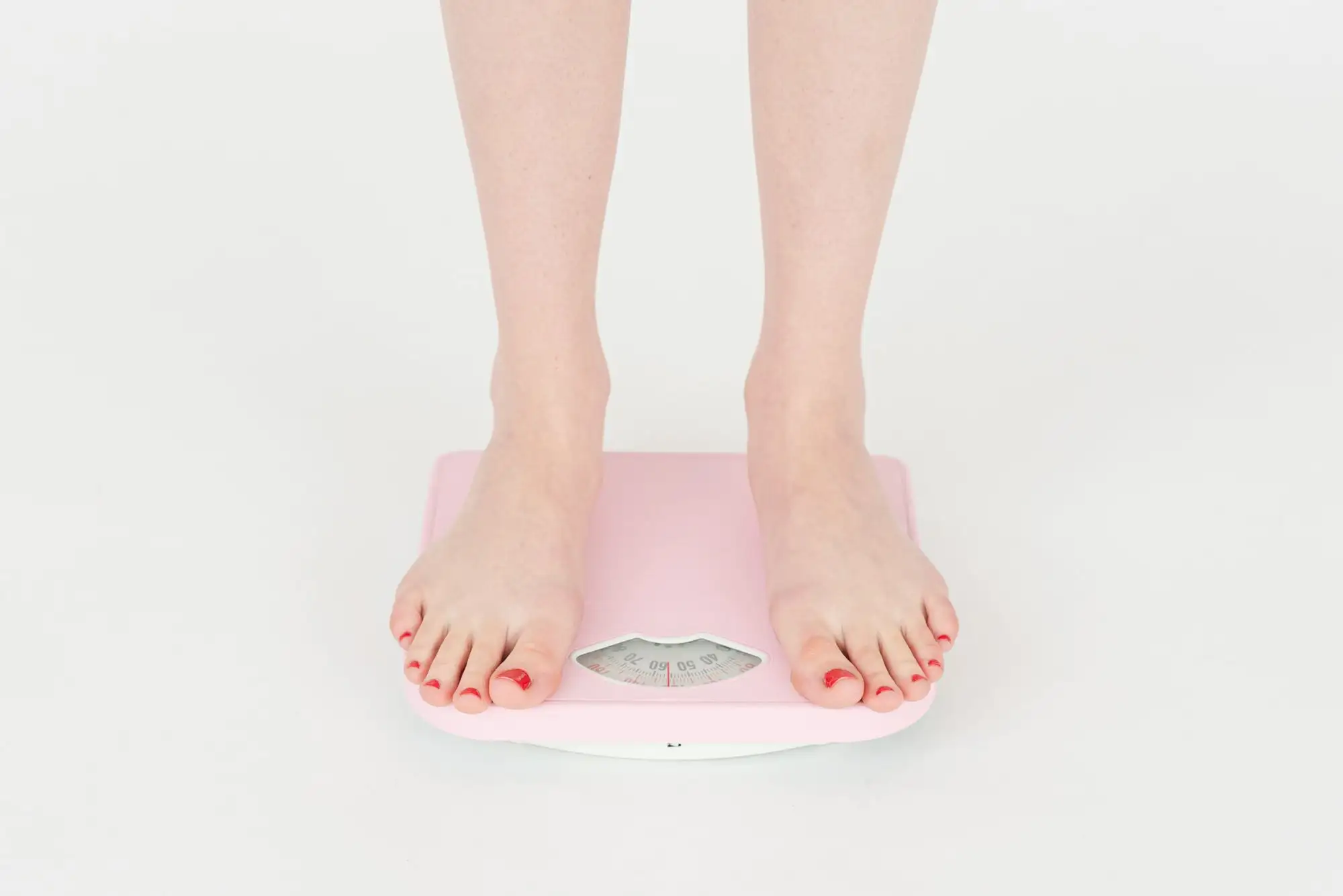 Bare feet stand on a pink bathroom scale.
