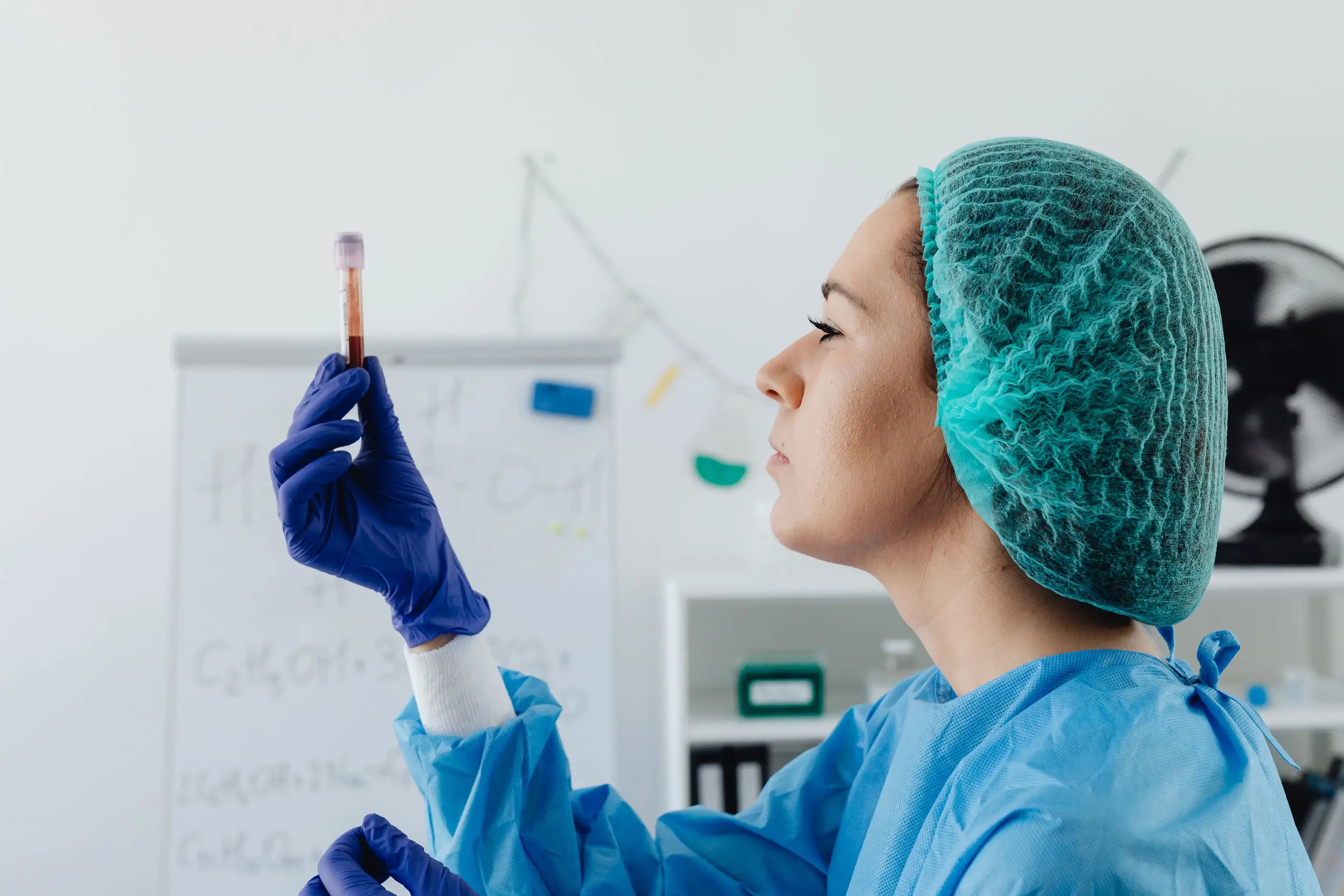 A laboratory worker in a hair cover checks a blood sample tube.