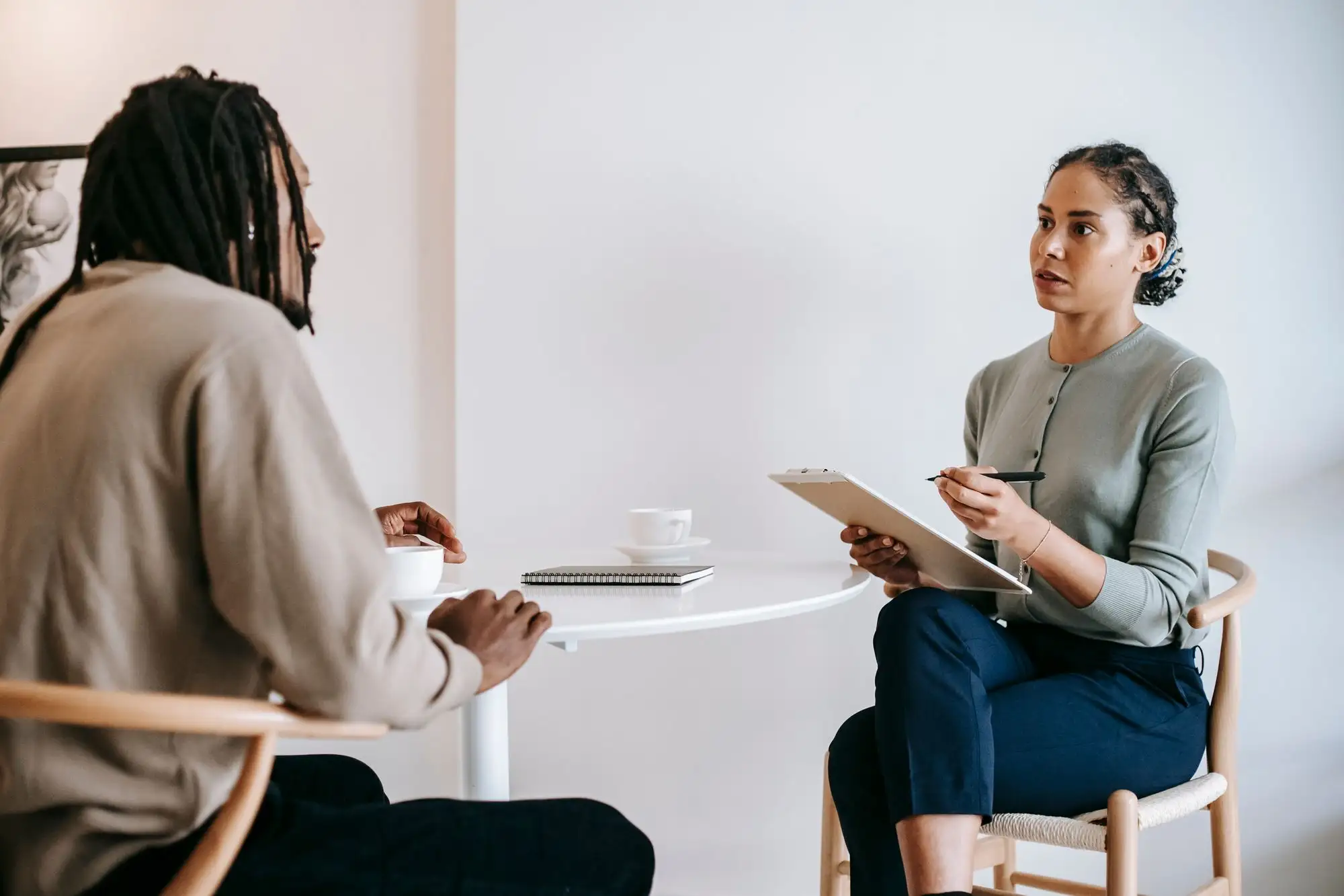 A woman with a clipboard interviews a candidate at a small table.