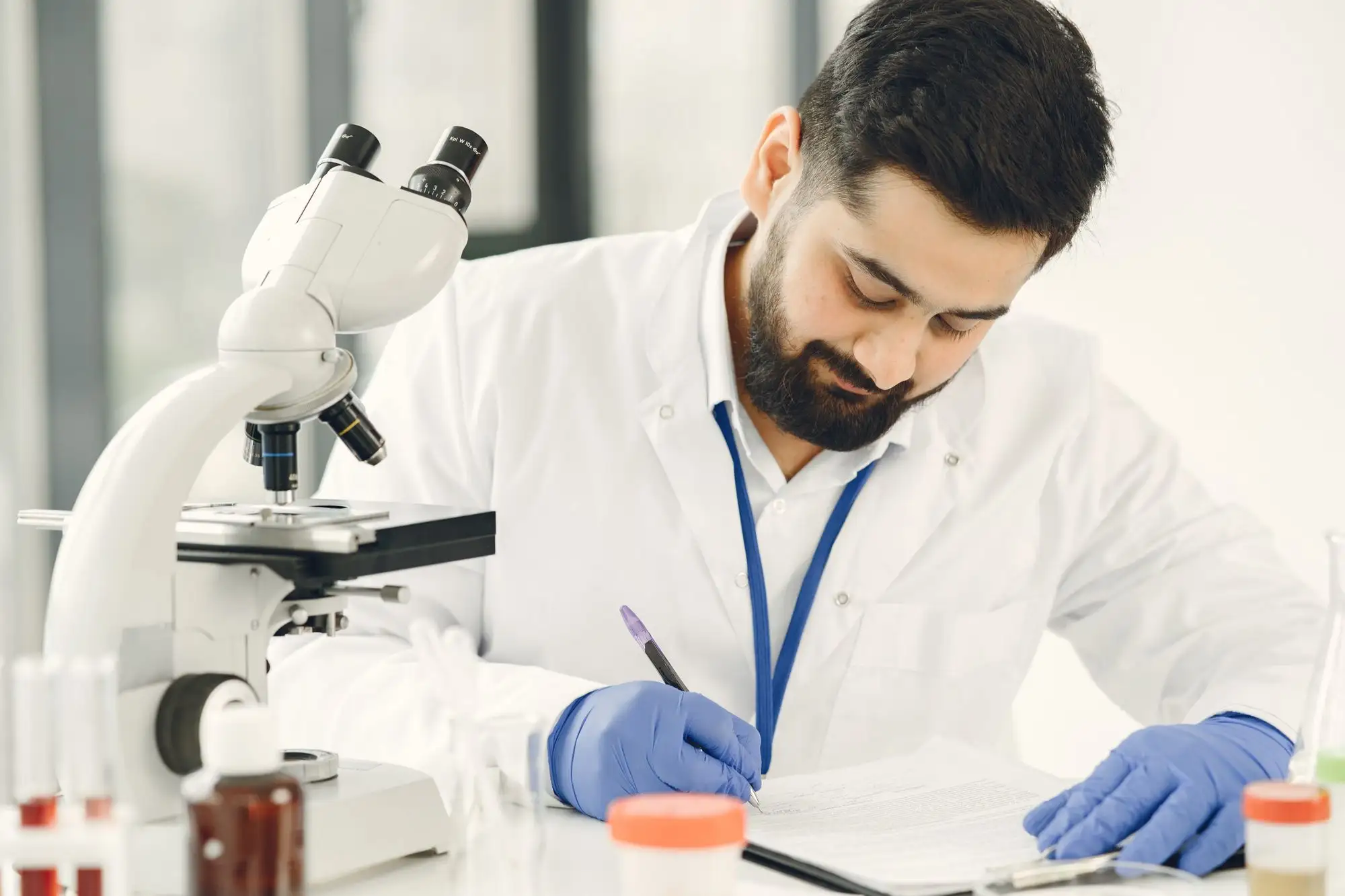 A scientist writes notes beside a microscope.