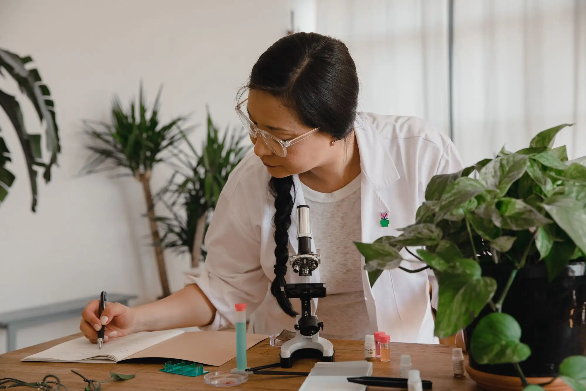 A student writes notes beside a microscope in a bright lab.