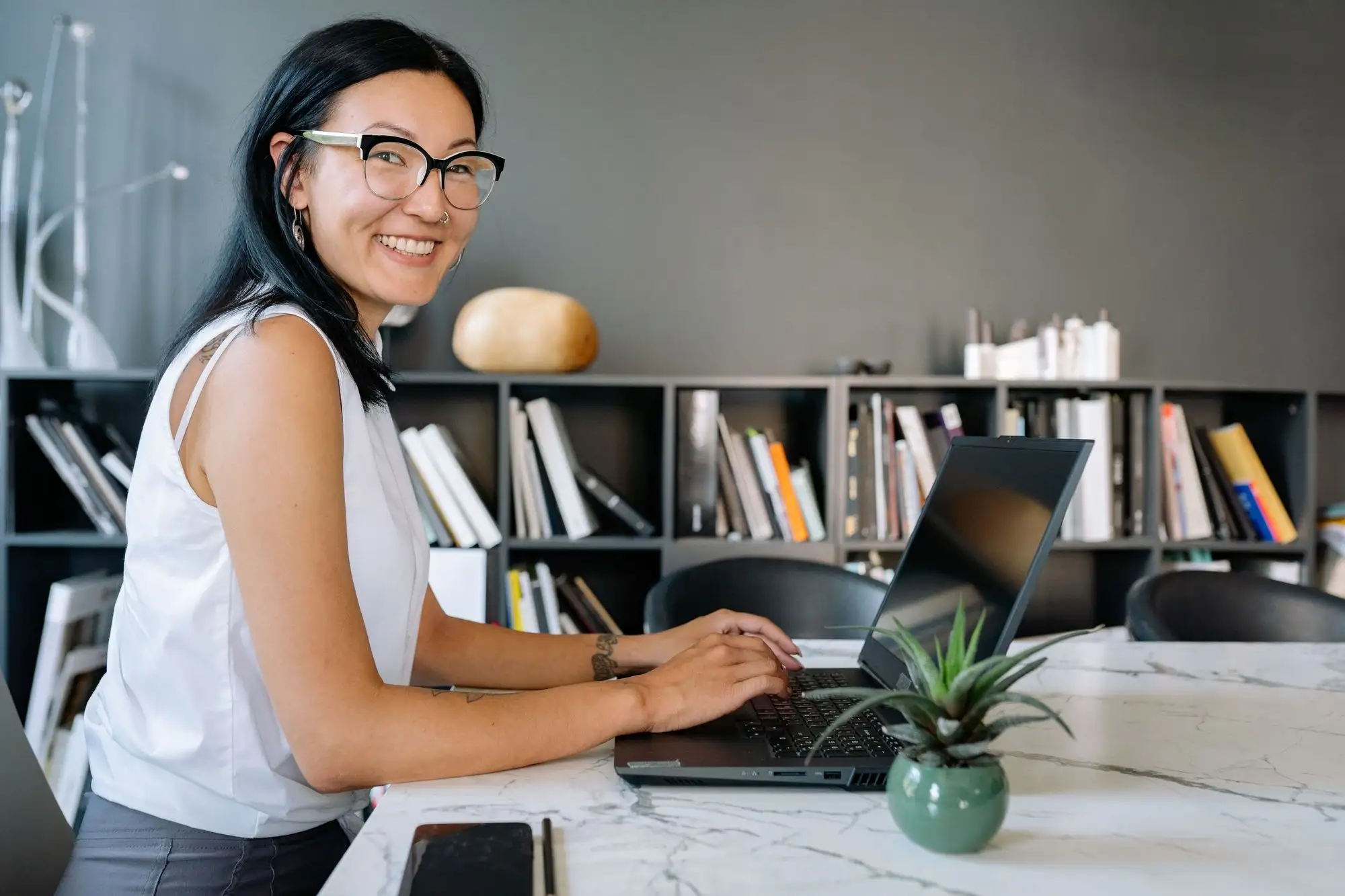 A smiling woman works at a laptop in a bright office.
