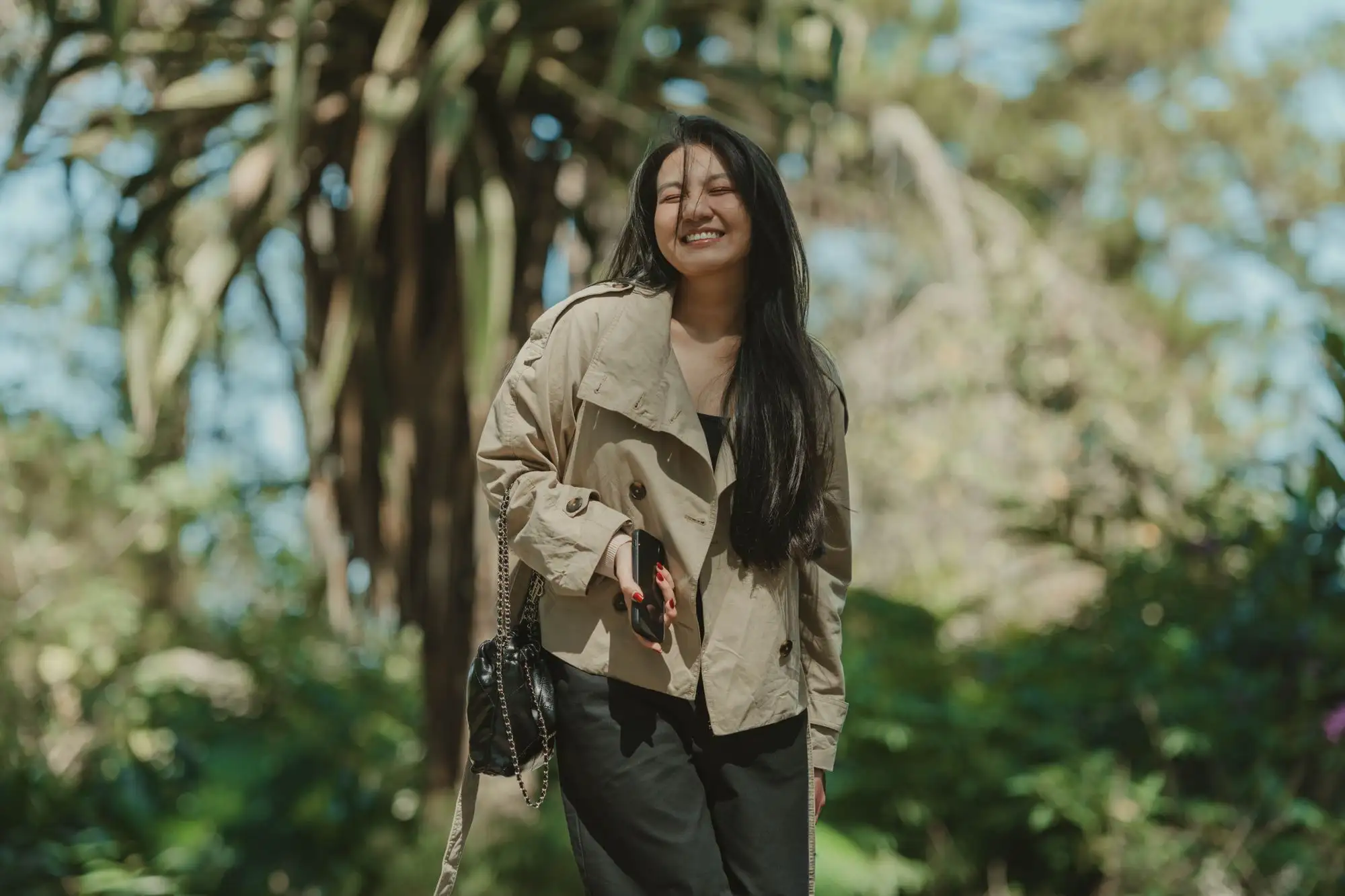 A woman laughs as she walks through a sunny park.