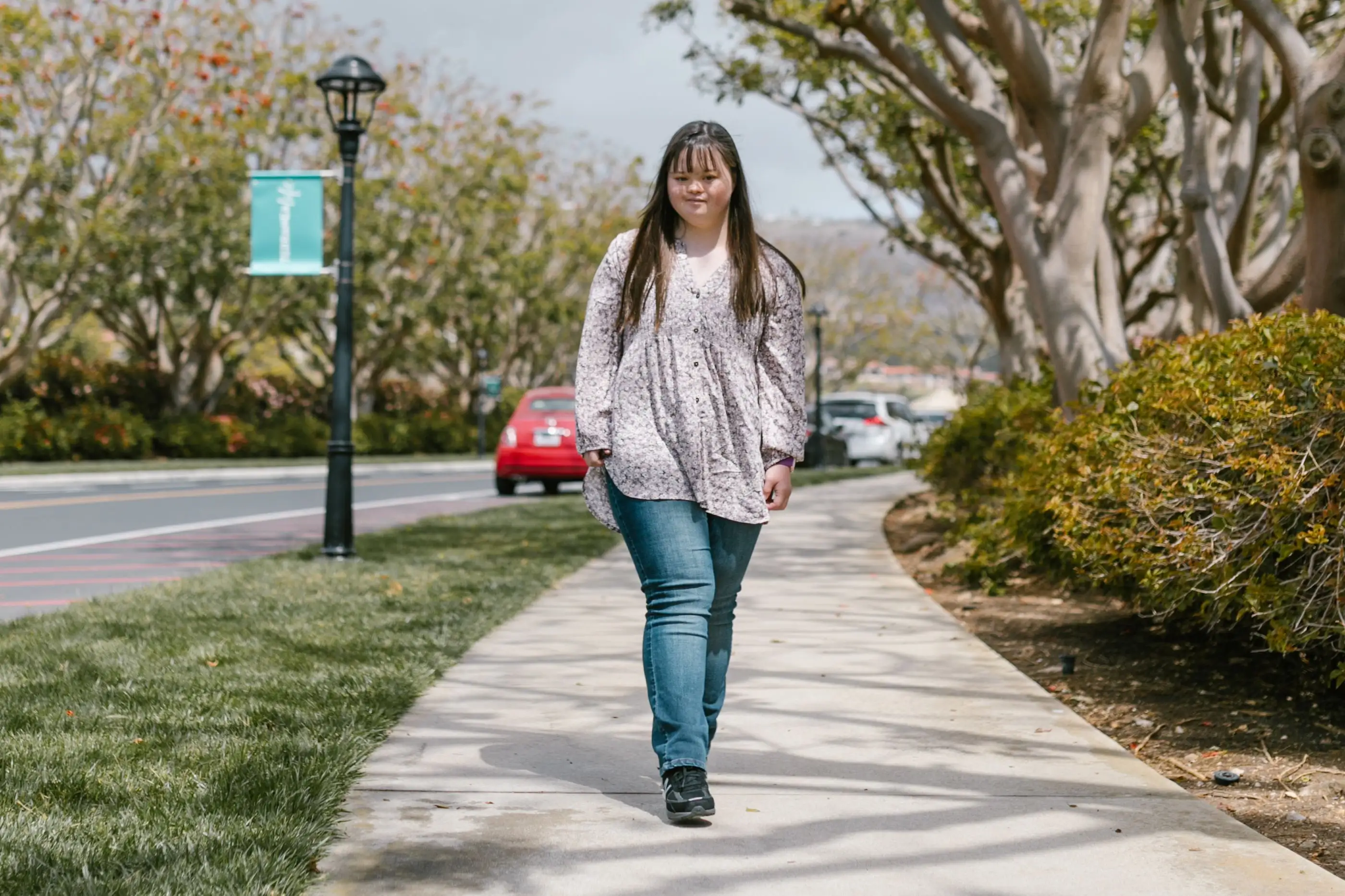 A woman walks along a tree-lined path.
