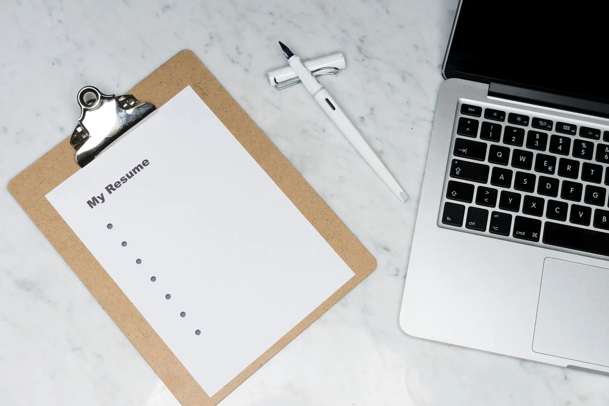 A blank resume on a clipboard sits beside a laptop.