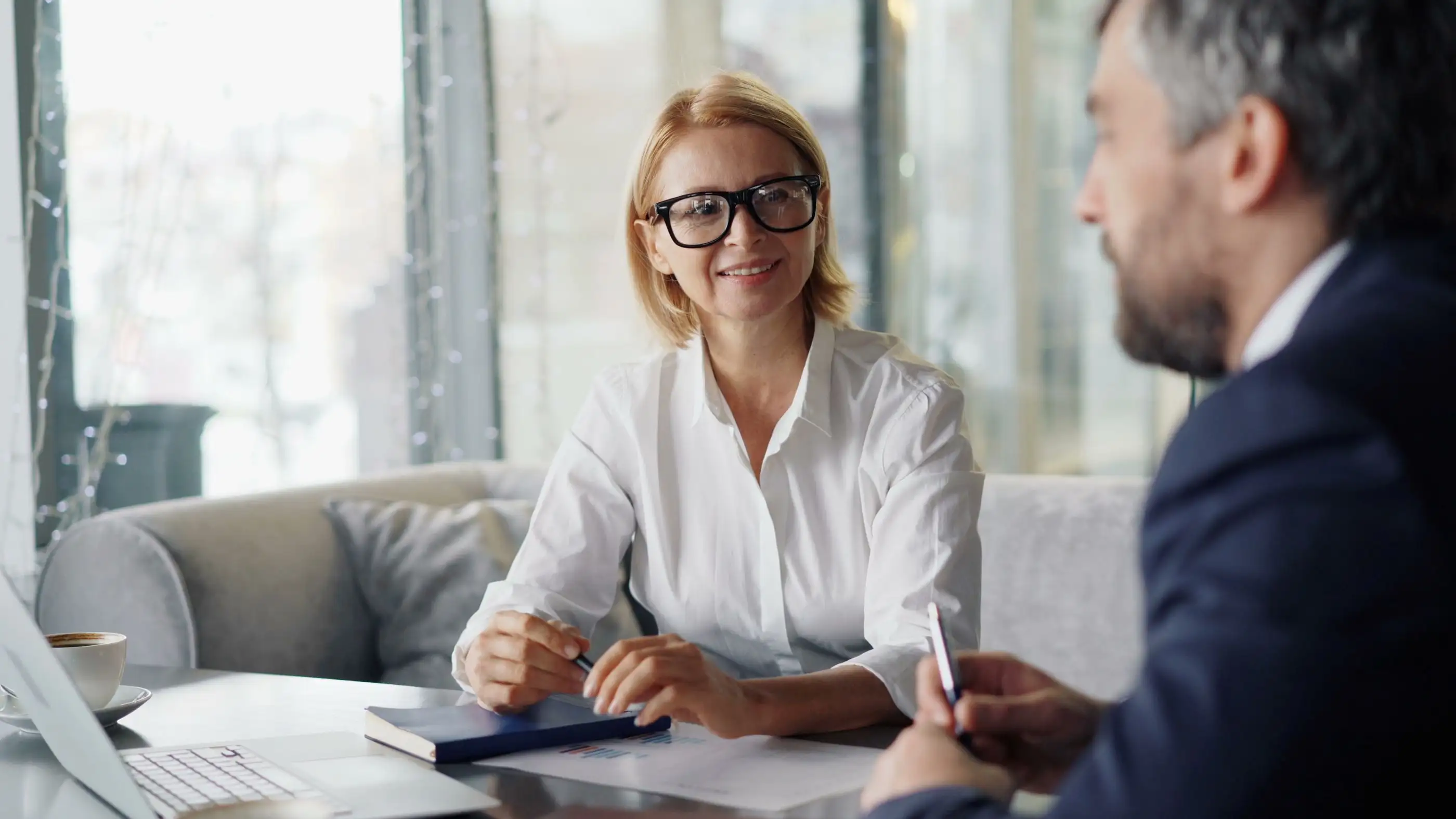 A smiling woman takes notes during a one-to-one meeting.