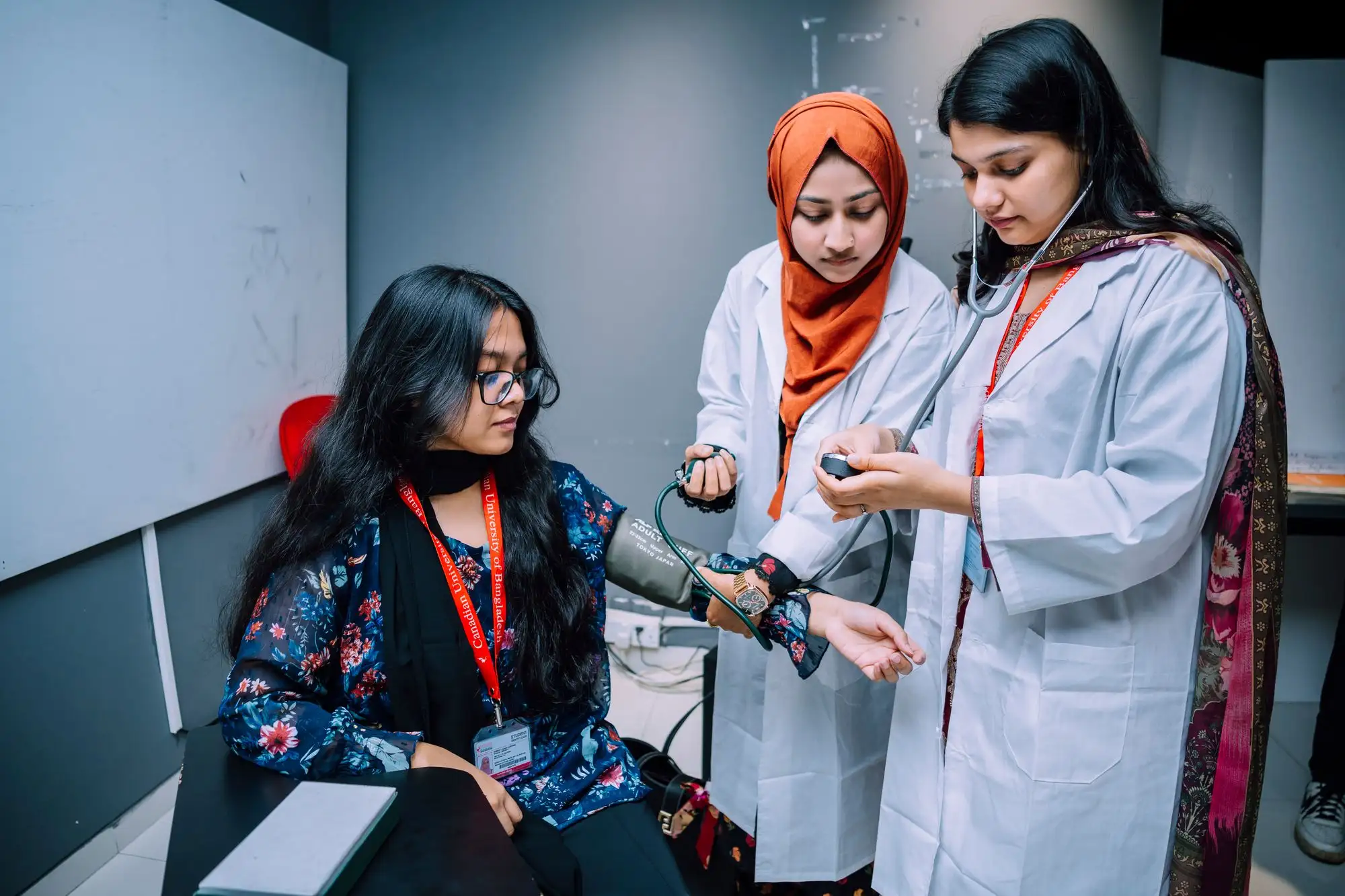 Two students in white coats practice taking a blood pressure reading.