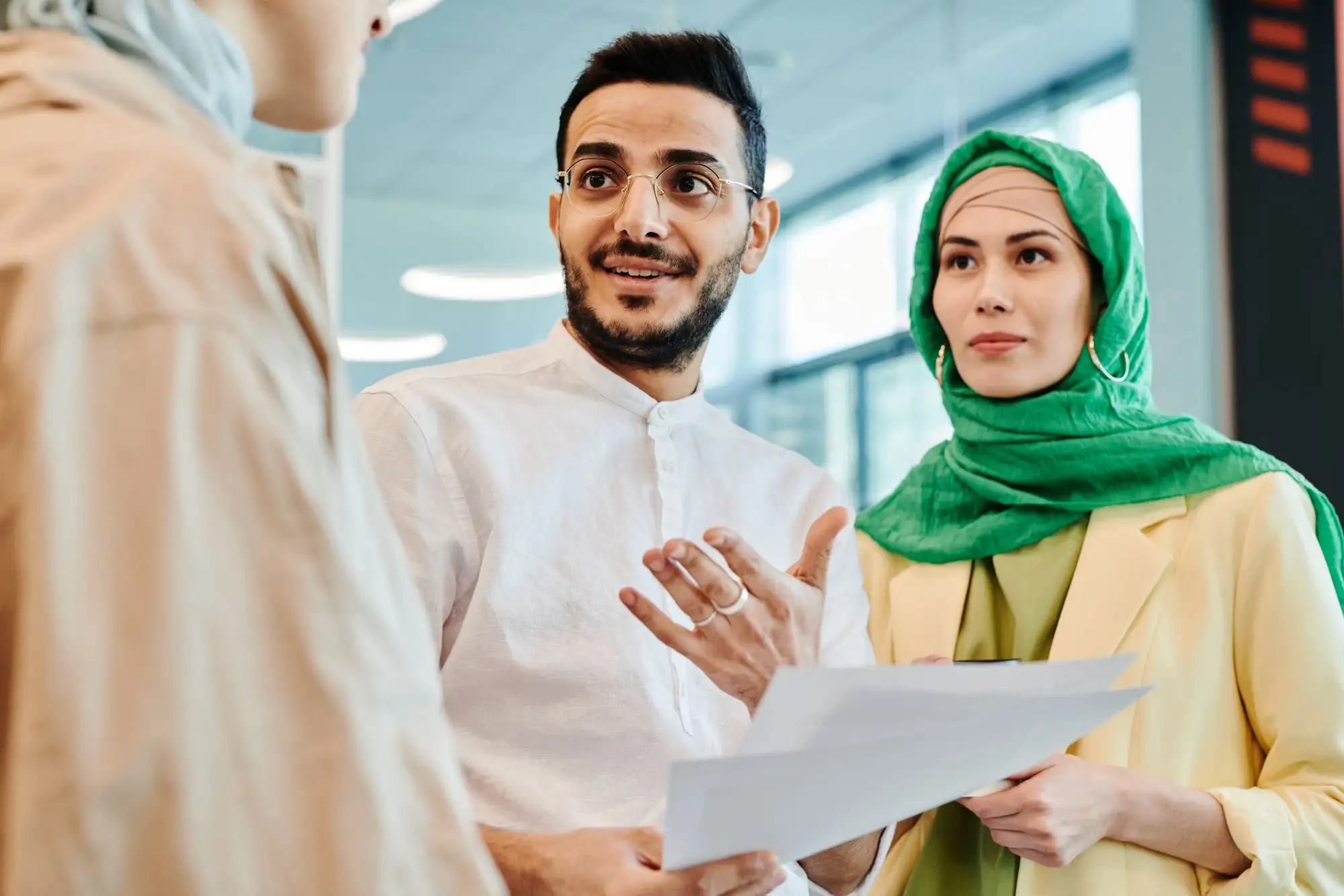A man explains a document to a colleague in a green headscarf.