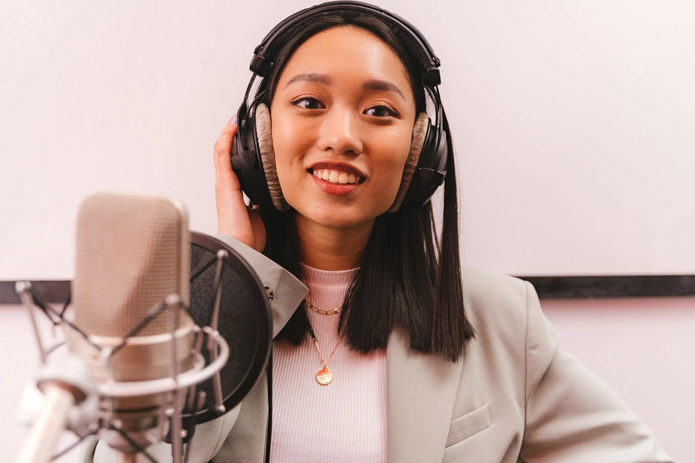 A smiling woman in headphones sits at a studio microphone.