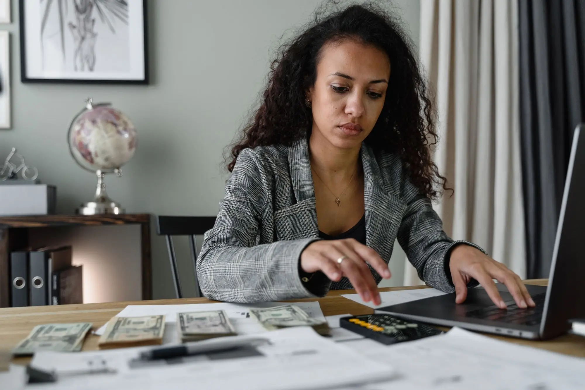 A woman works through figures on her laptop beside a calculator and papers.
