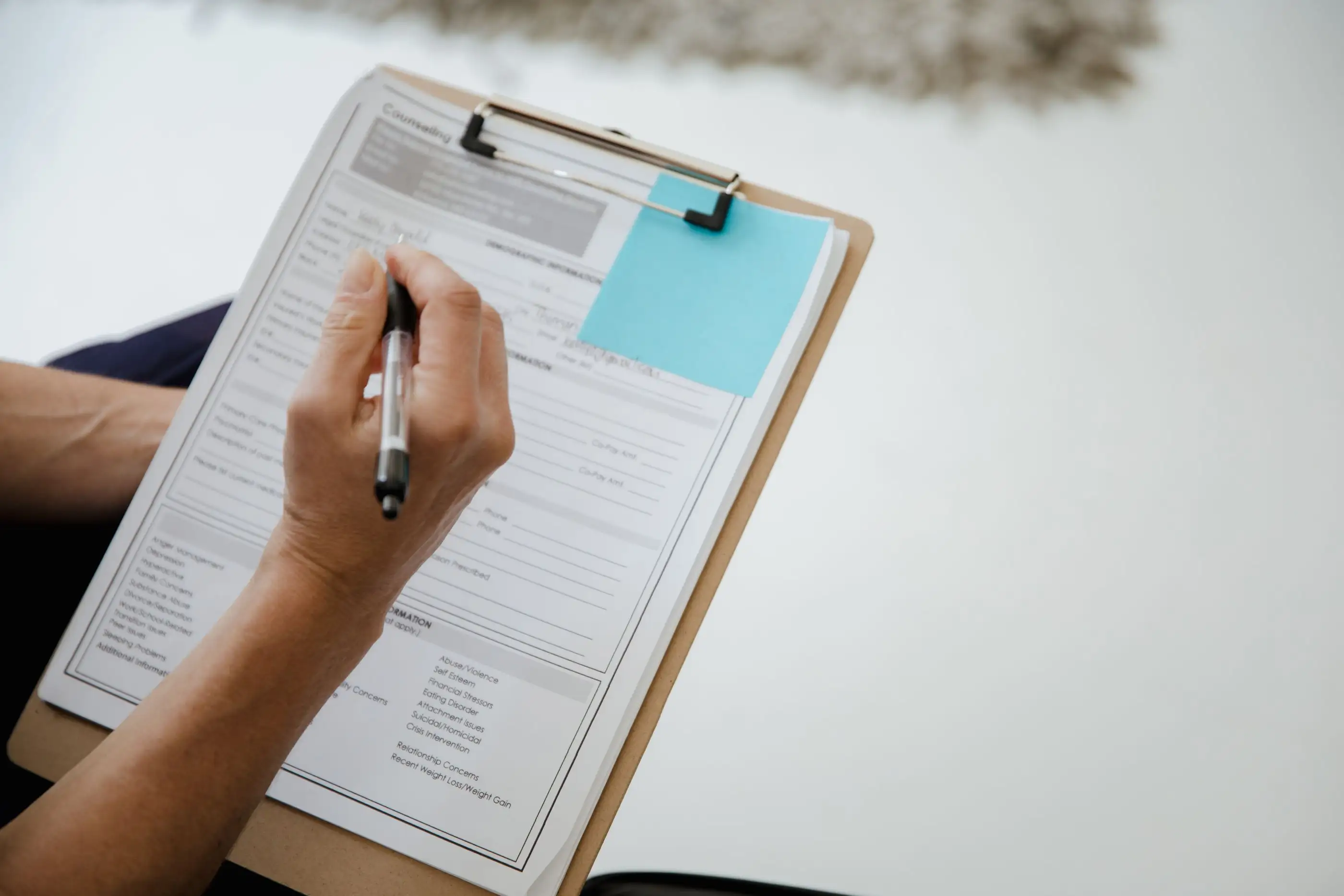 A hand fills in an application form on a clipboard.
