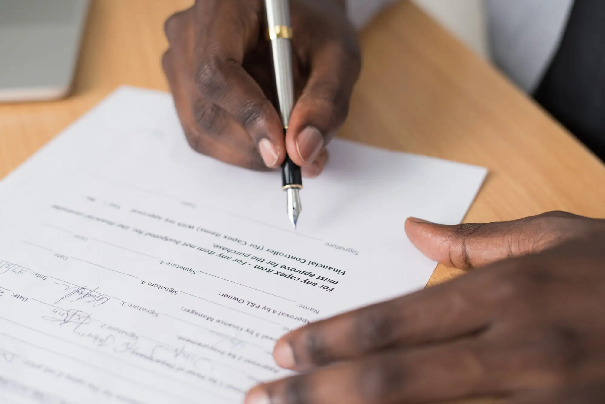 A hand signs a printed form while another hand steadies the page.