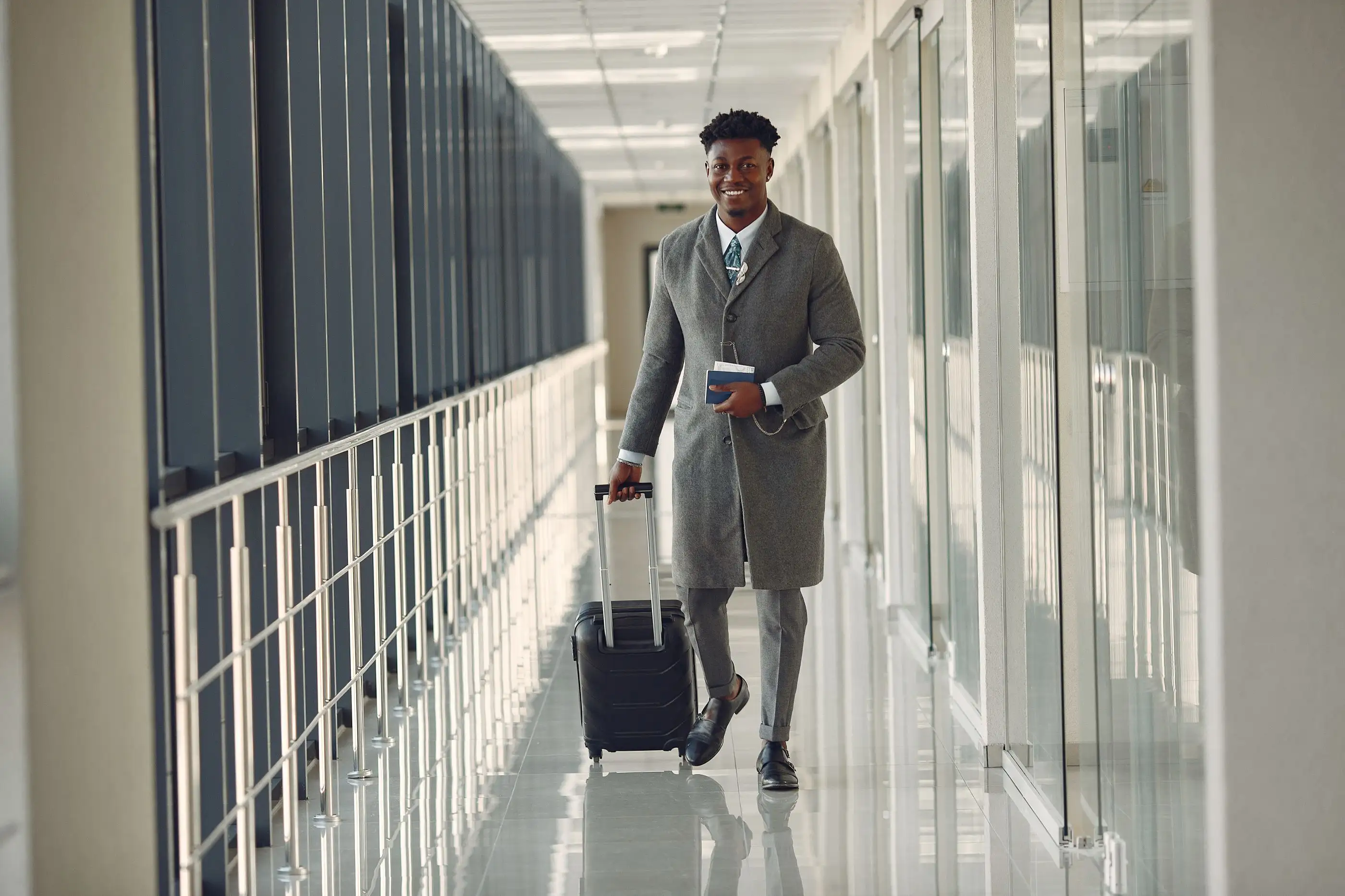 A traveler walks with his suitcase along a glass airport corridor.