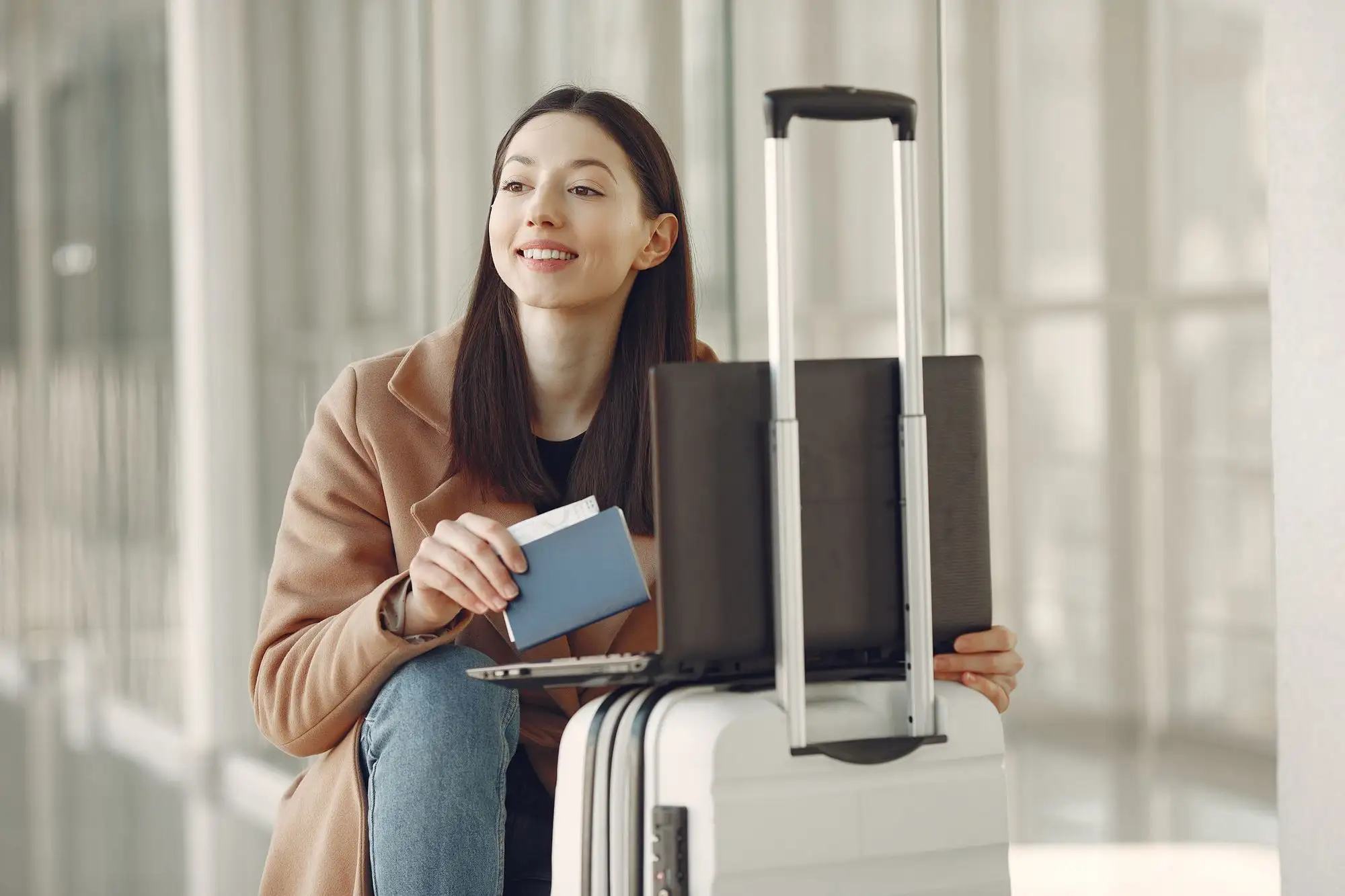 A young woman with a suitcase smiles while waiting at an airport.
