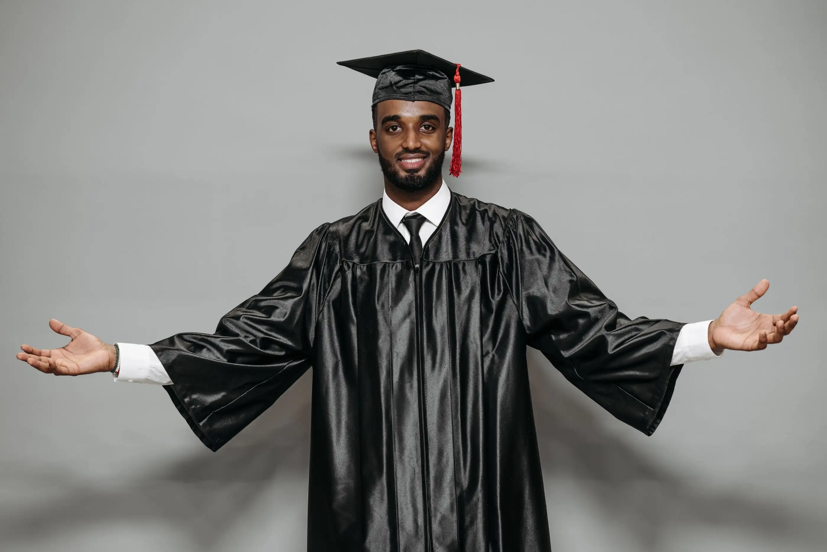 A smiling graduate in cap and gown opens his arms.