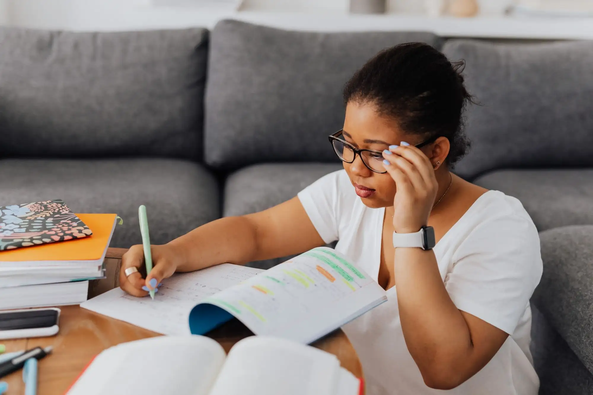A student in glasses studies a highlighted workbook on a sofa.