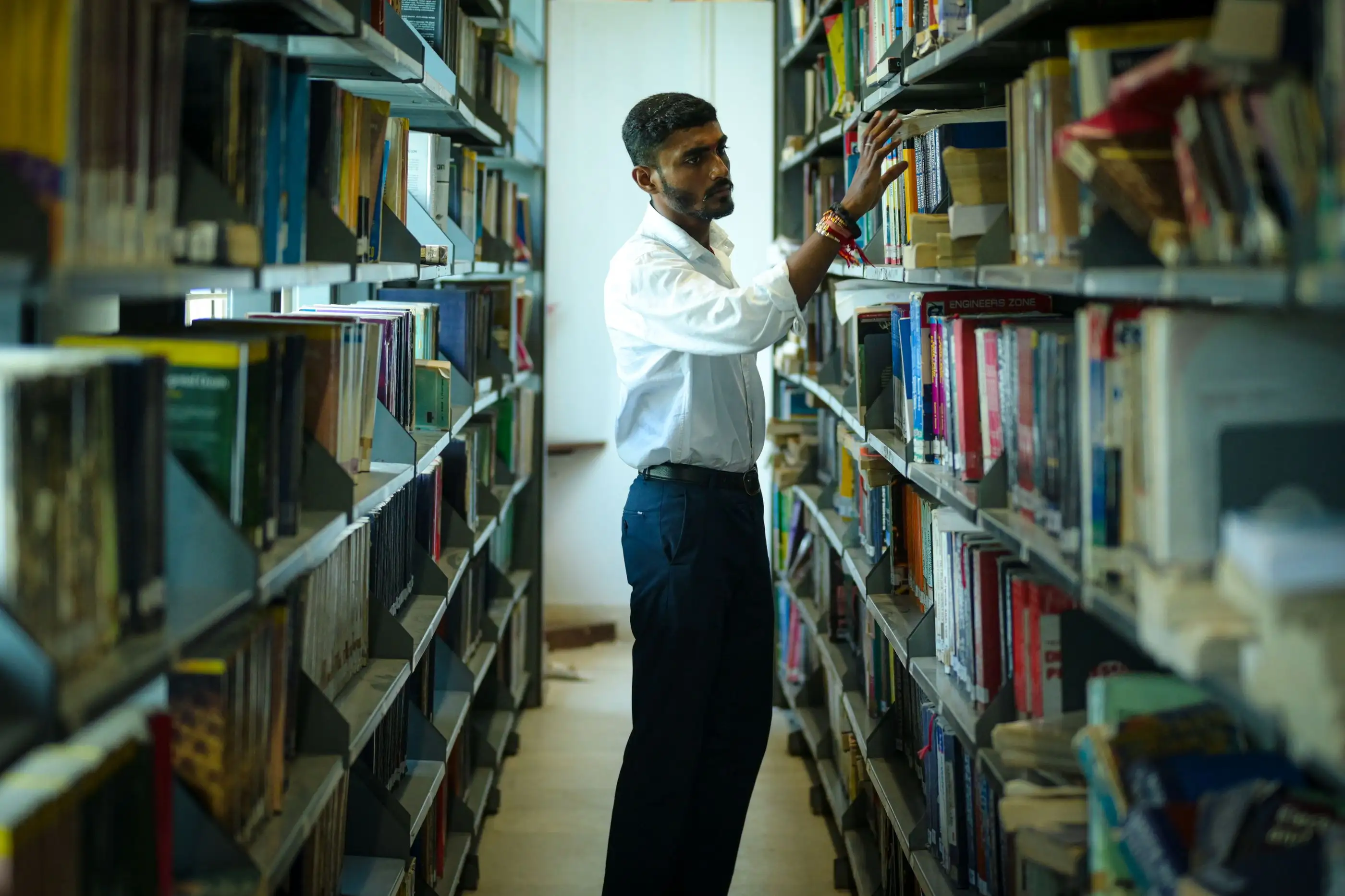 A student looks for a book between library shelves.