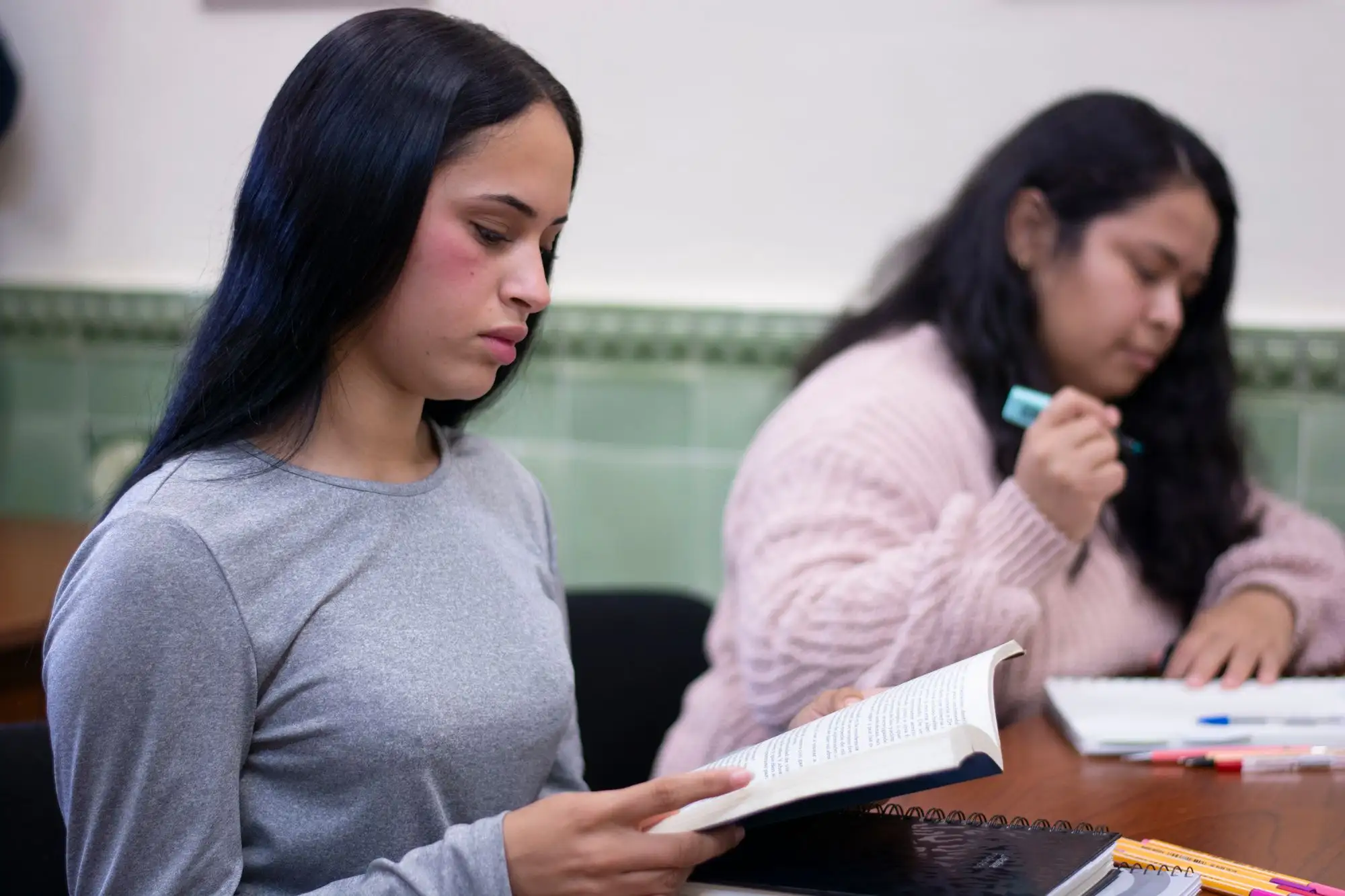 Two students read and take notes at a shared table.