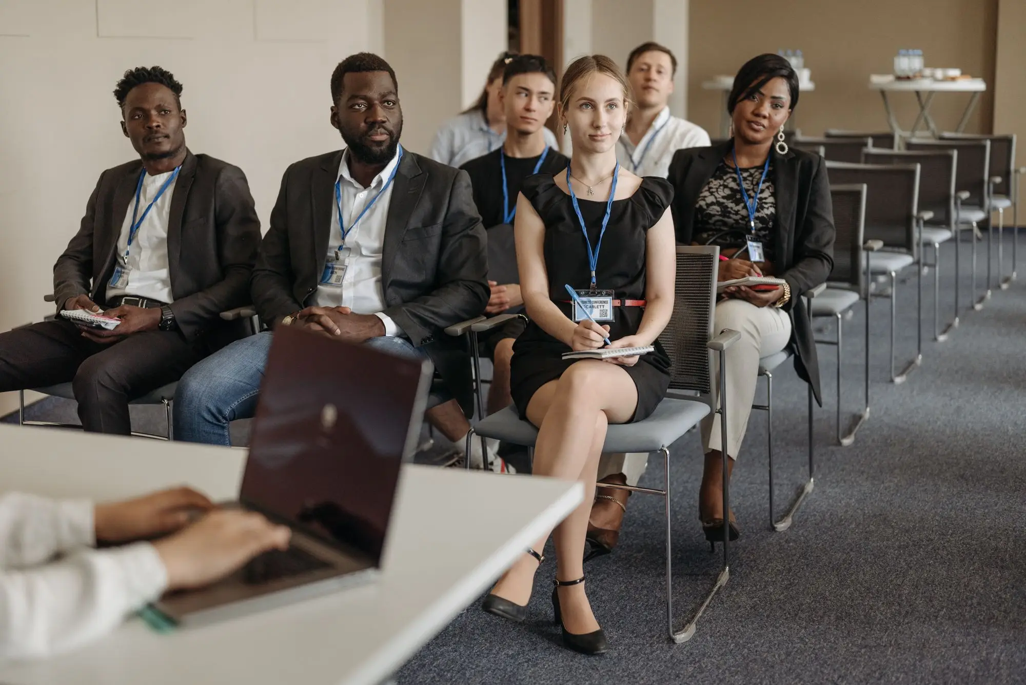 Professionals with name badges listen and take notes at a conference session.