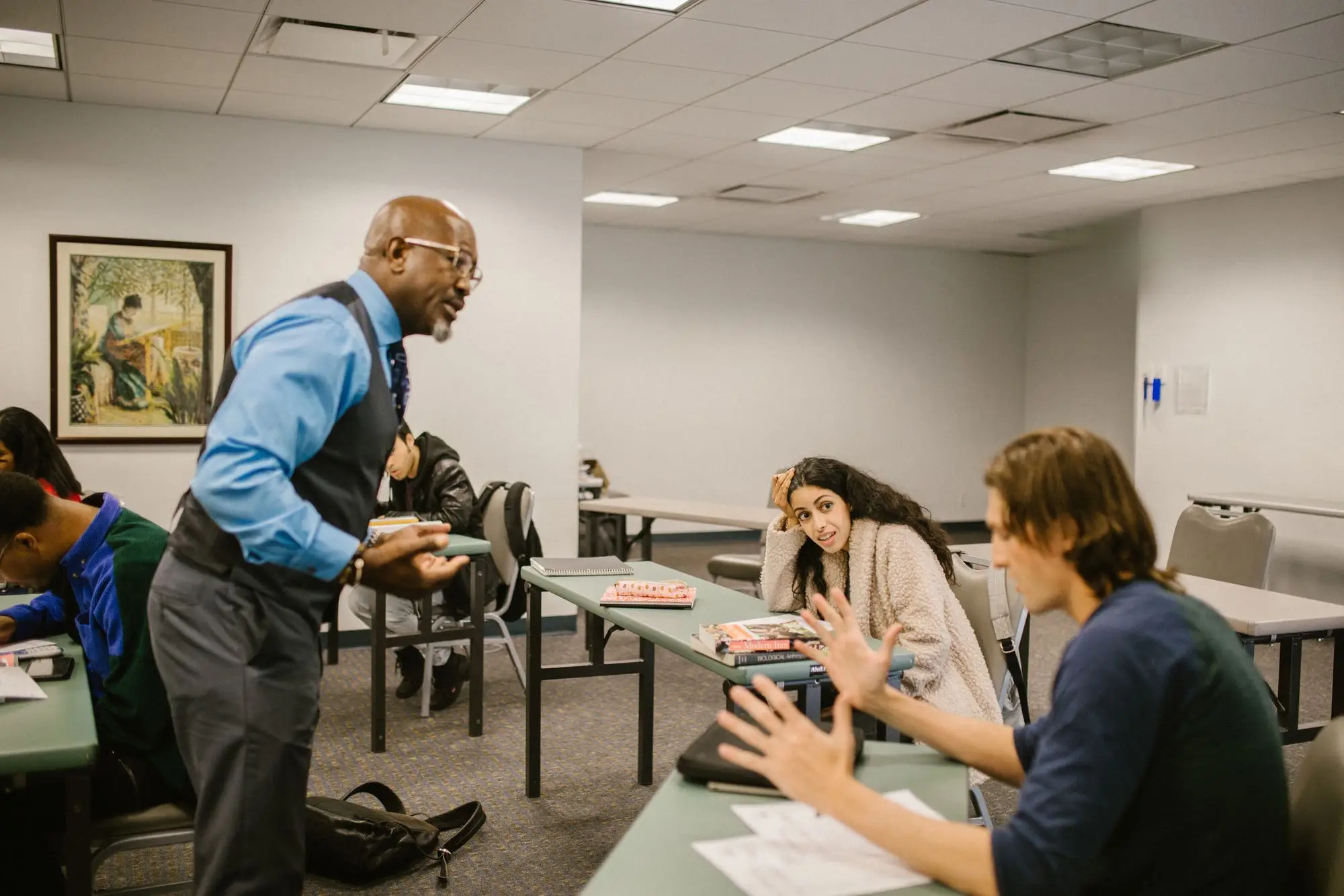 An instructor talks with students around their desks in a classroom.