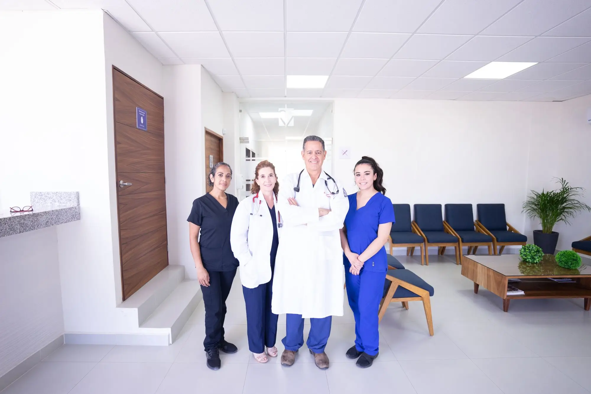 A pharmacist, a physician and two nurses stand together in a bright clinic lobby.