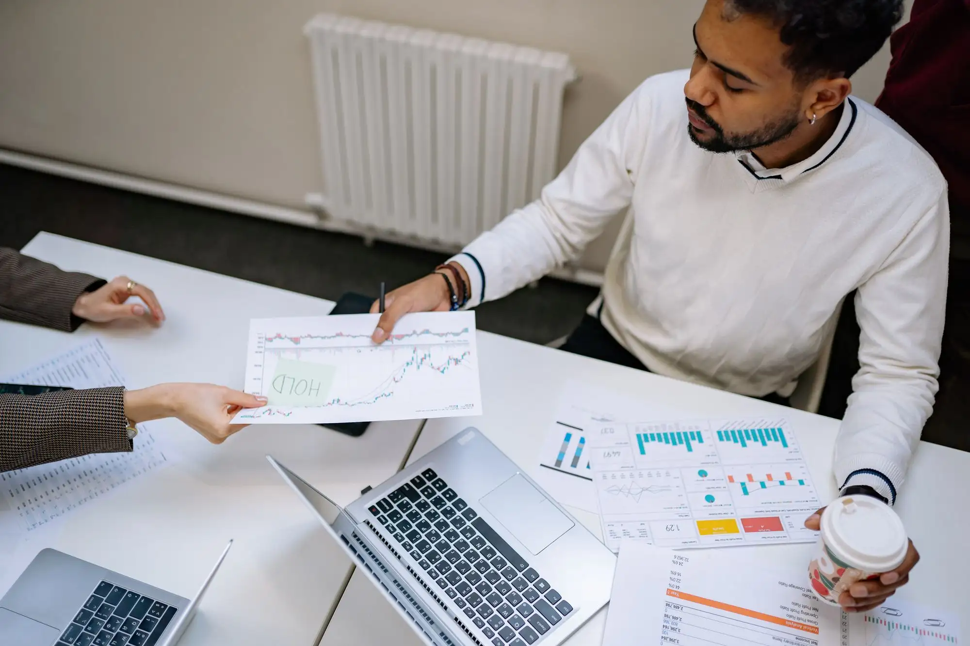 A man hands a colleague a printed chart across a desk.