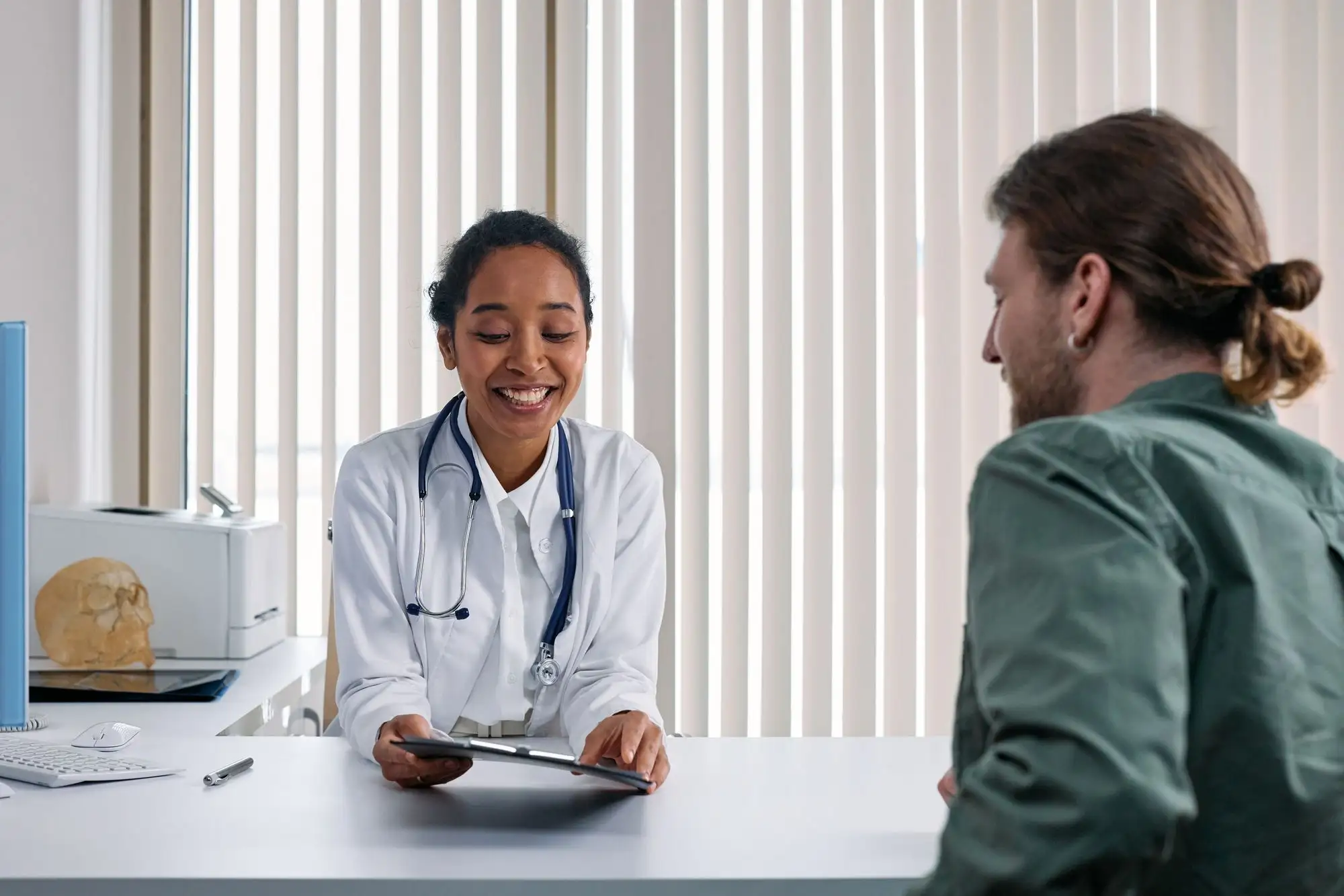 A smiling clinician reviews information with a patient across her desk.