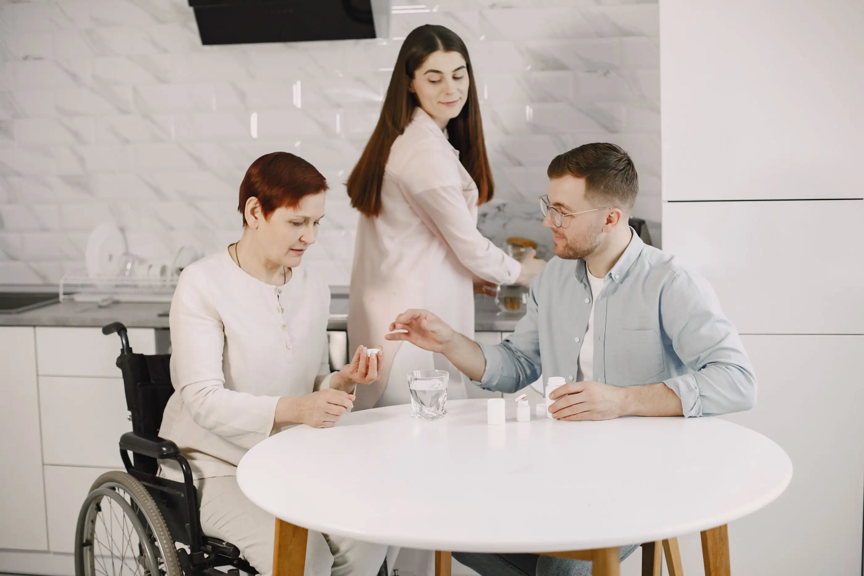 A family sits at a kitchen table while a woman hands out tablets and water.
