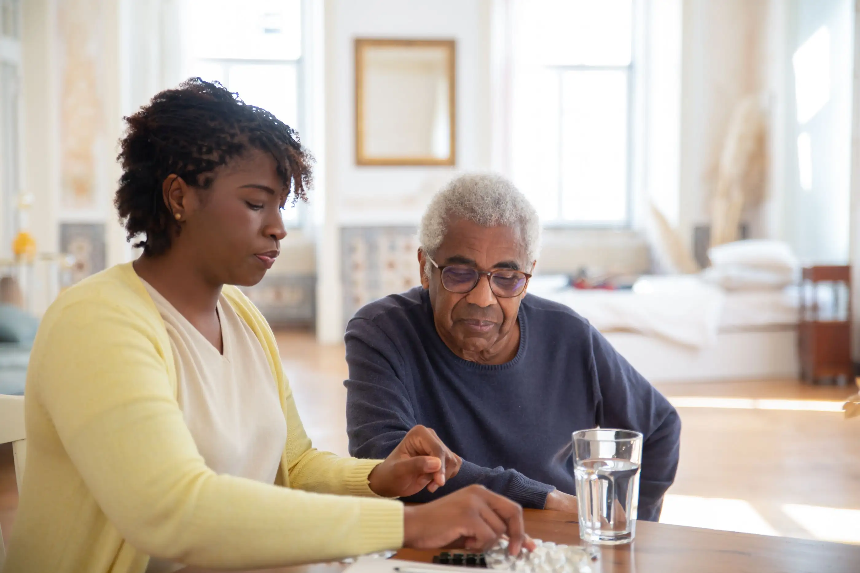 A woman helps an older man sort his tablets at the dining table.