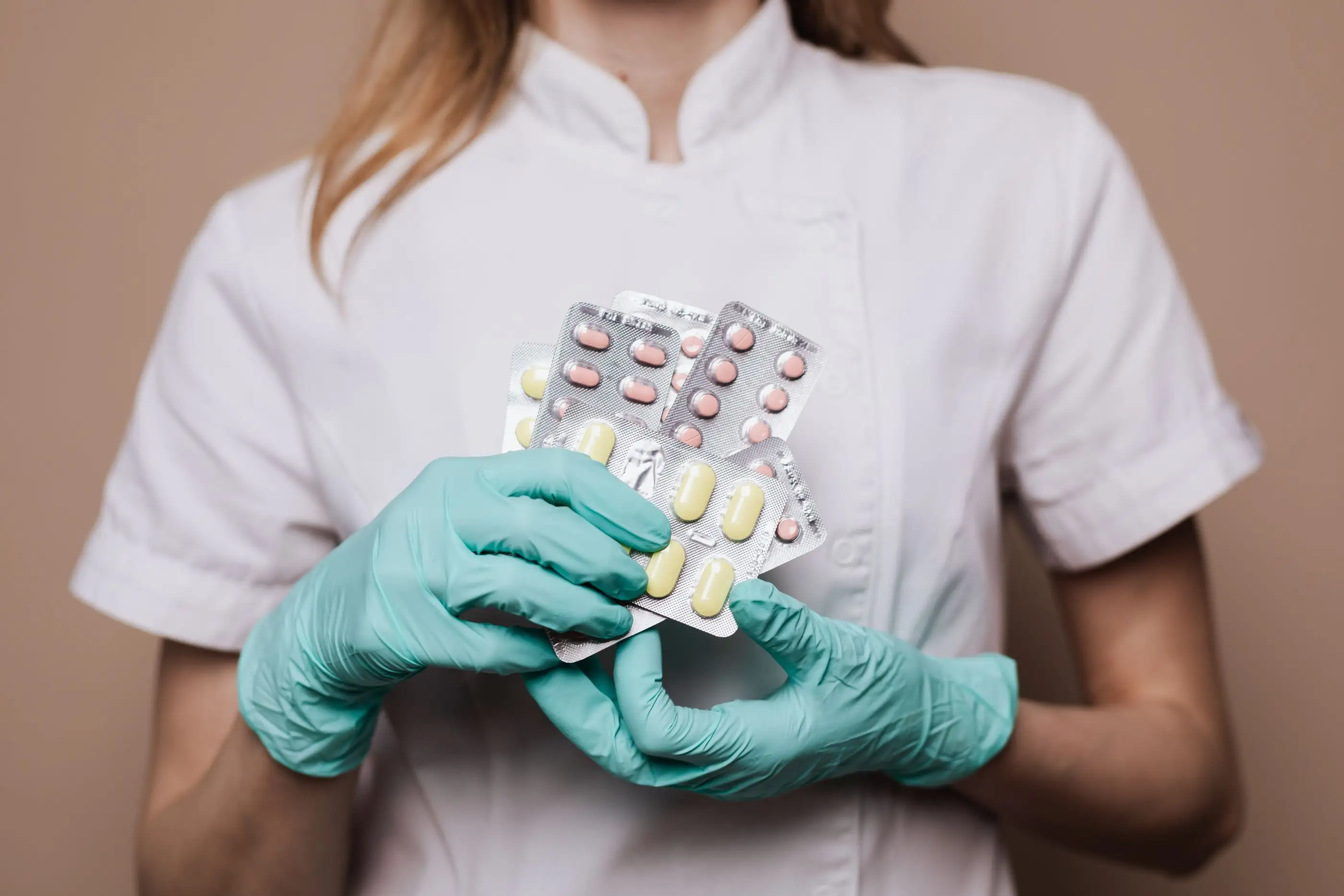 Gloved hands hold several blister packs of tablets.