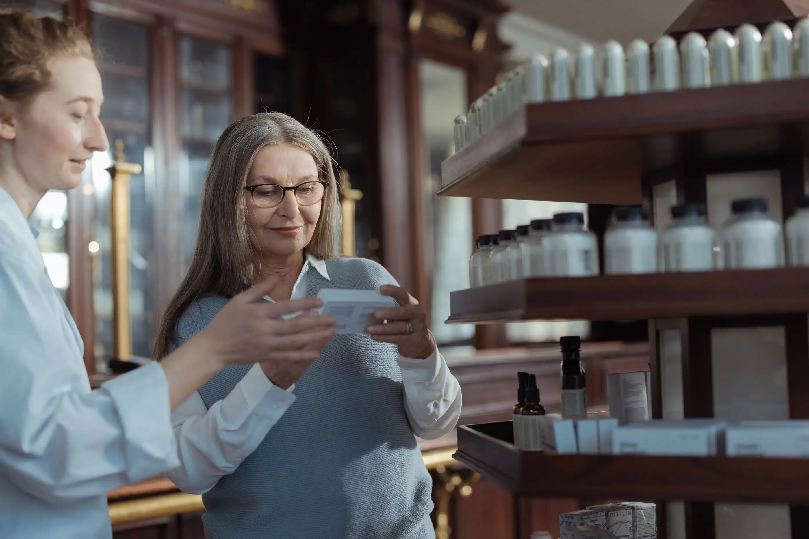 A pharmacist hands a smiling older woman her medicine at the counter.
