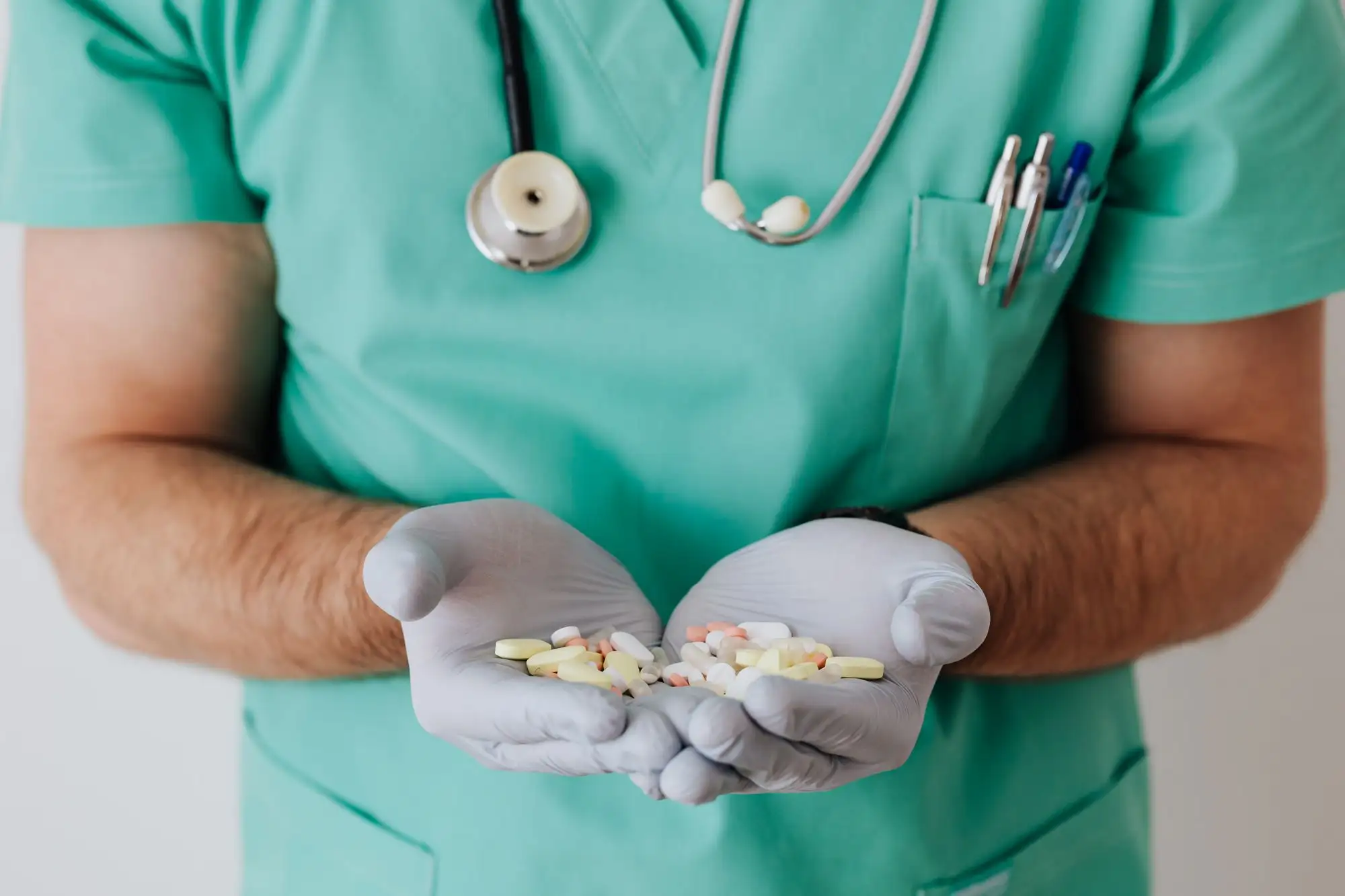 A clinician in scrubs holds tablets in cupped, gloved hands.