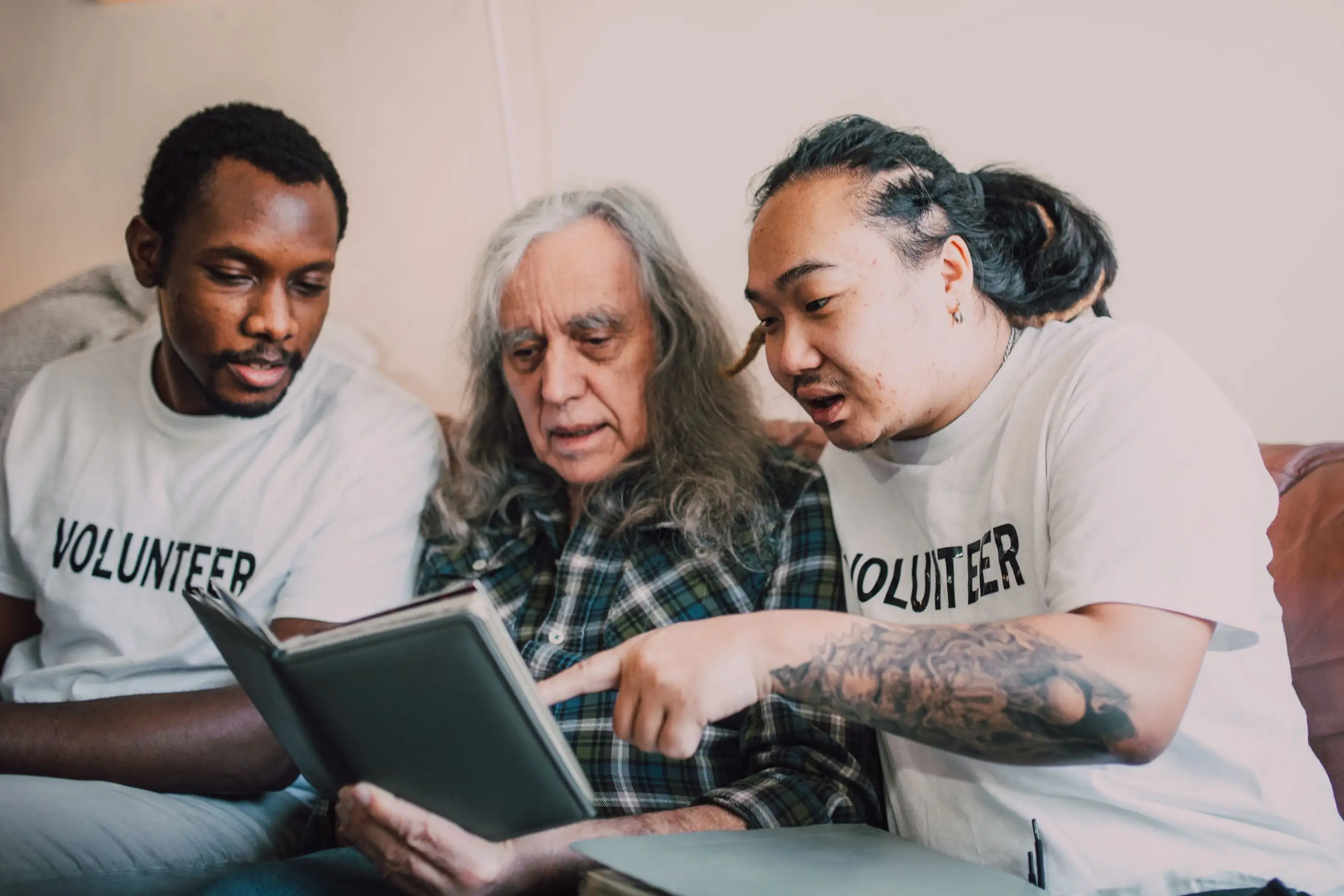 Two volunteers read a book with an older man.