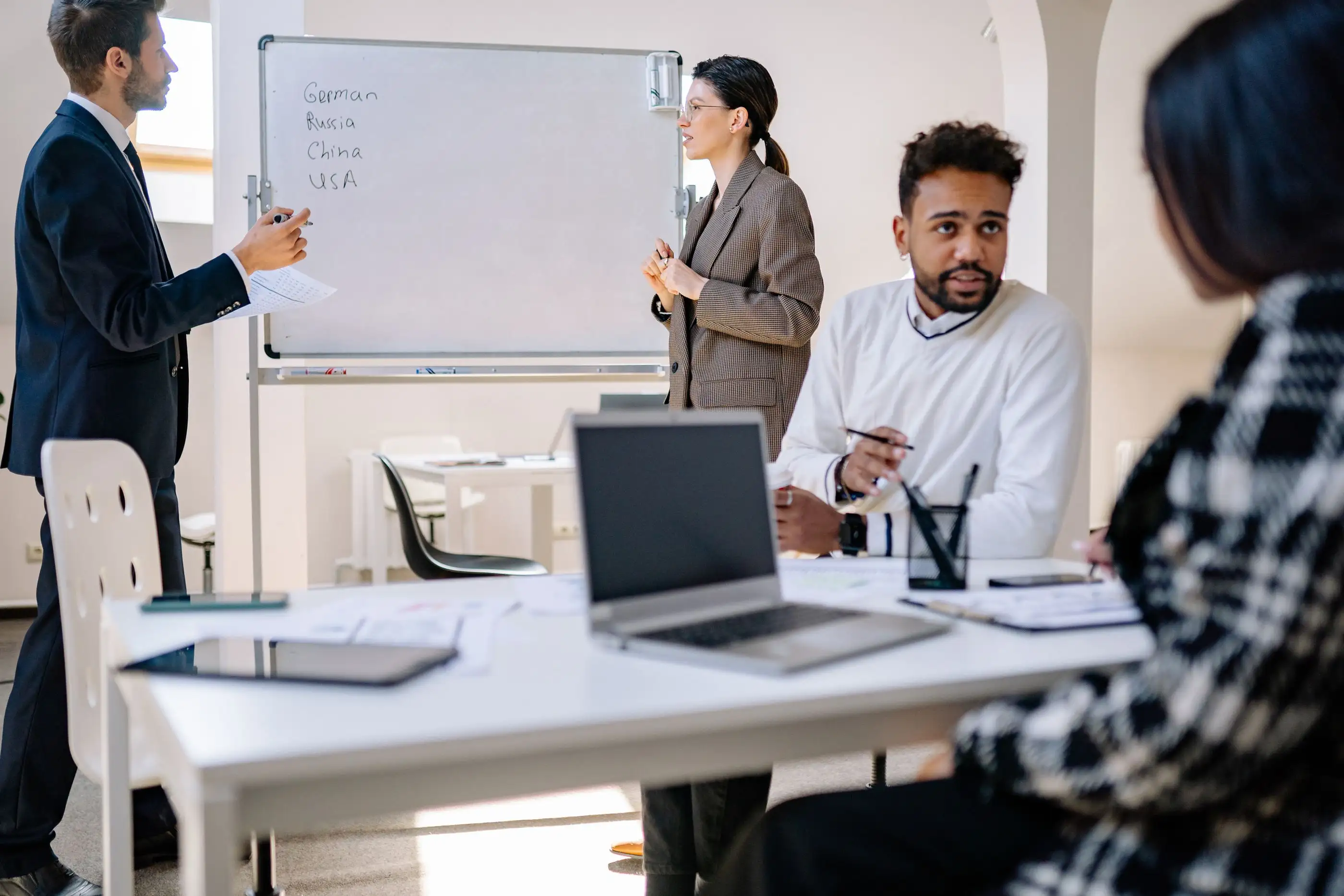 A team meets around a table while a colleague writes on a whiteboard.