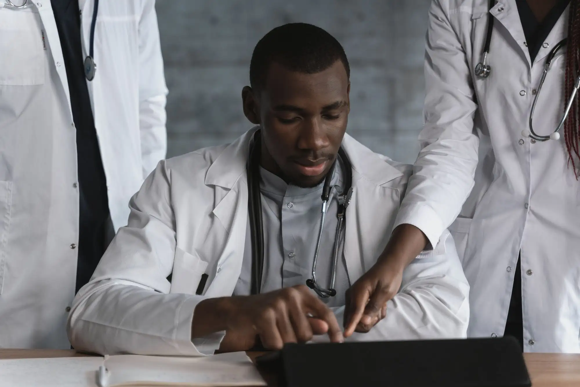A physician writes notes while a colleague looks on.