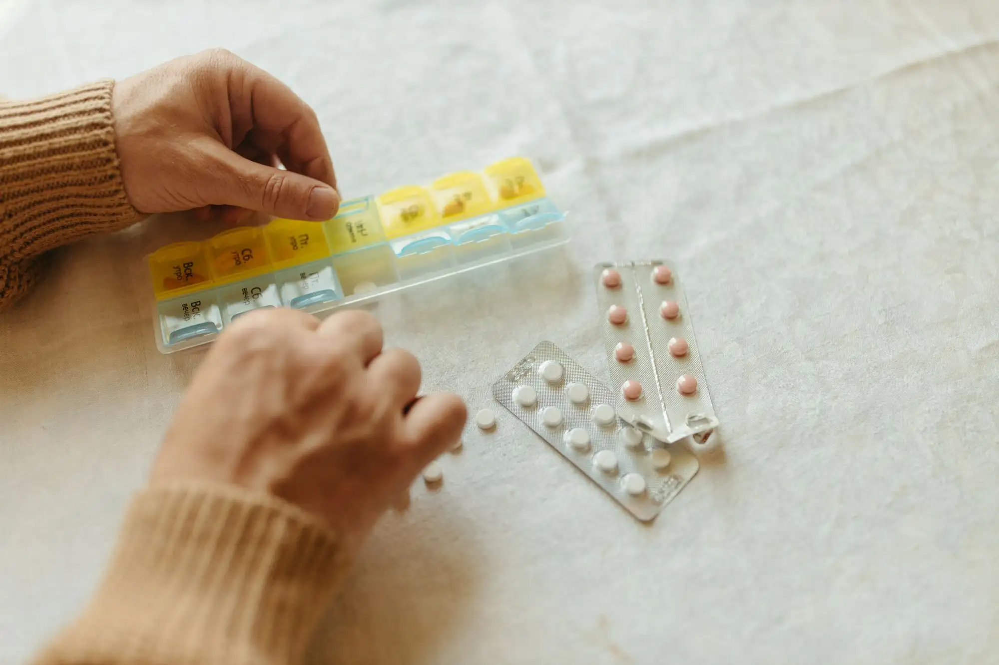 Hands fill a weekly pill organizer beside blister packs.