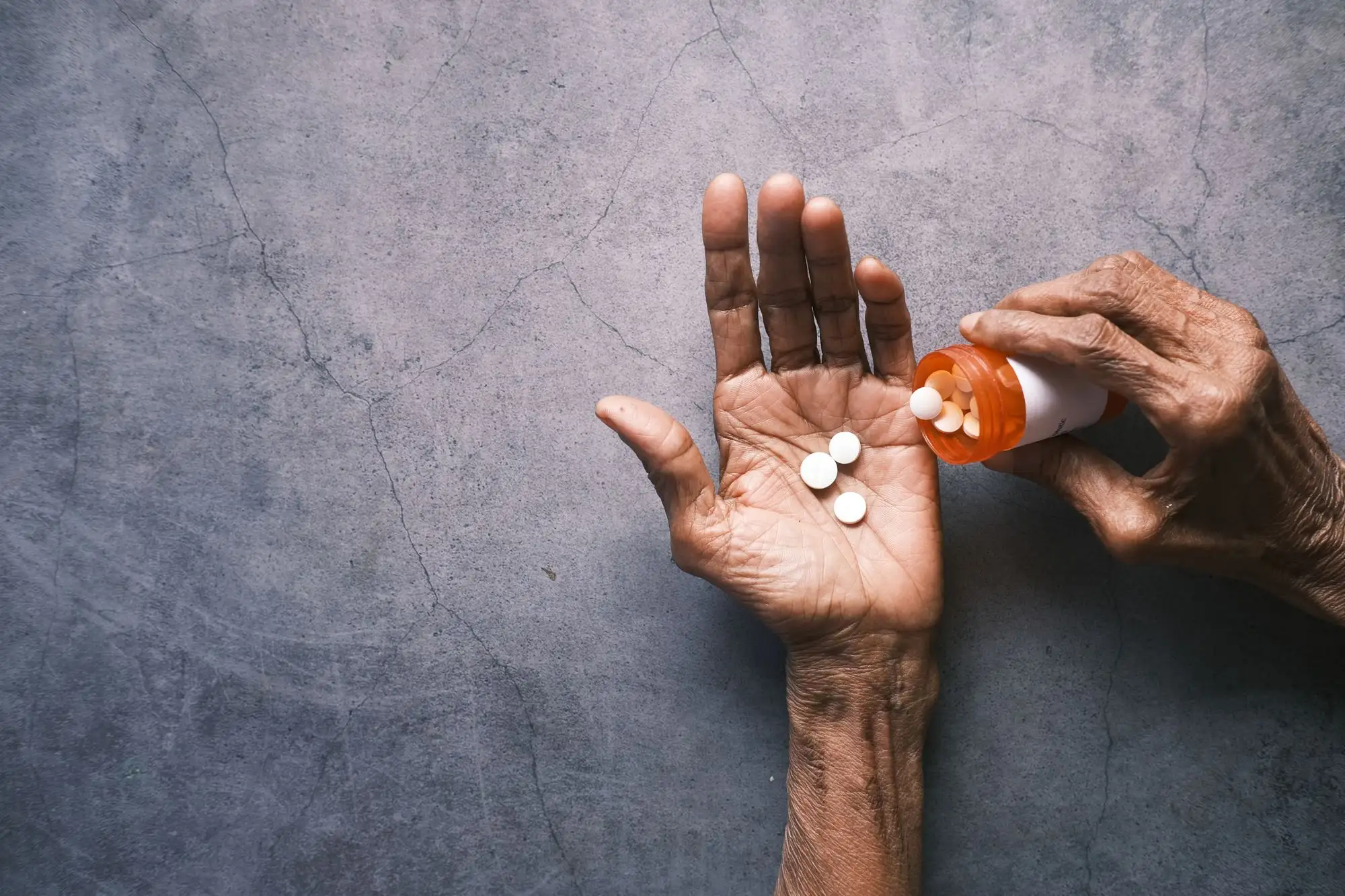 An older person pours tablets from a bottle into the palm of a hand.