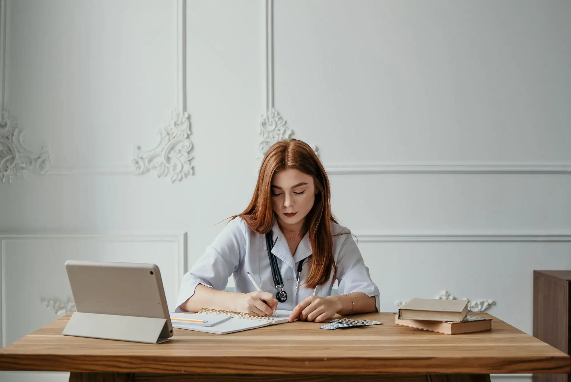 A clinician writes notes at a desk with a tablet and books.