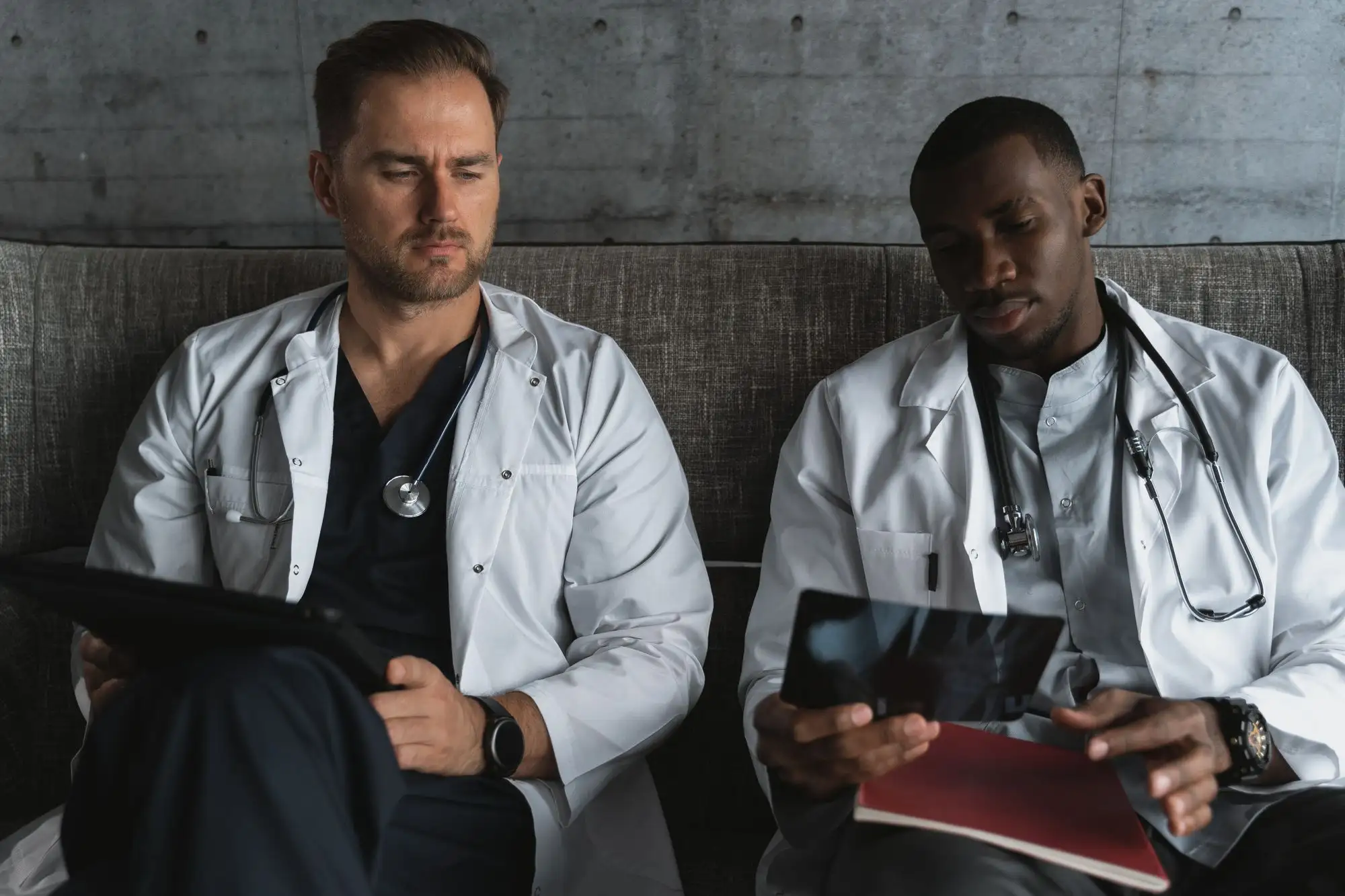Two physicians review notes and images together on a sofa.
