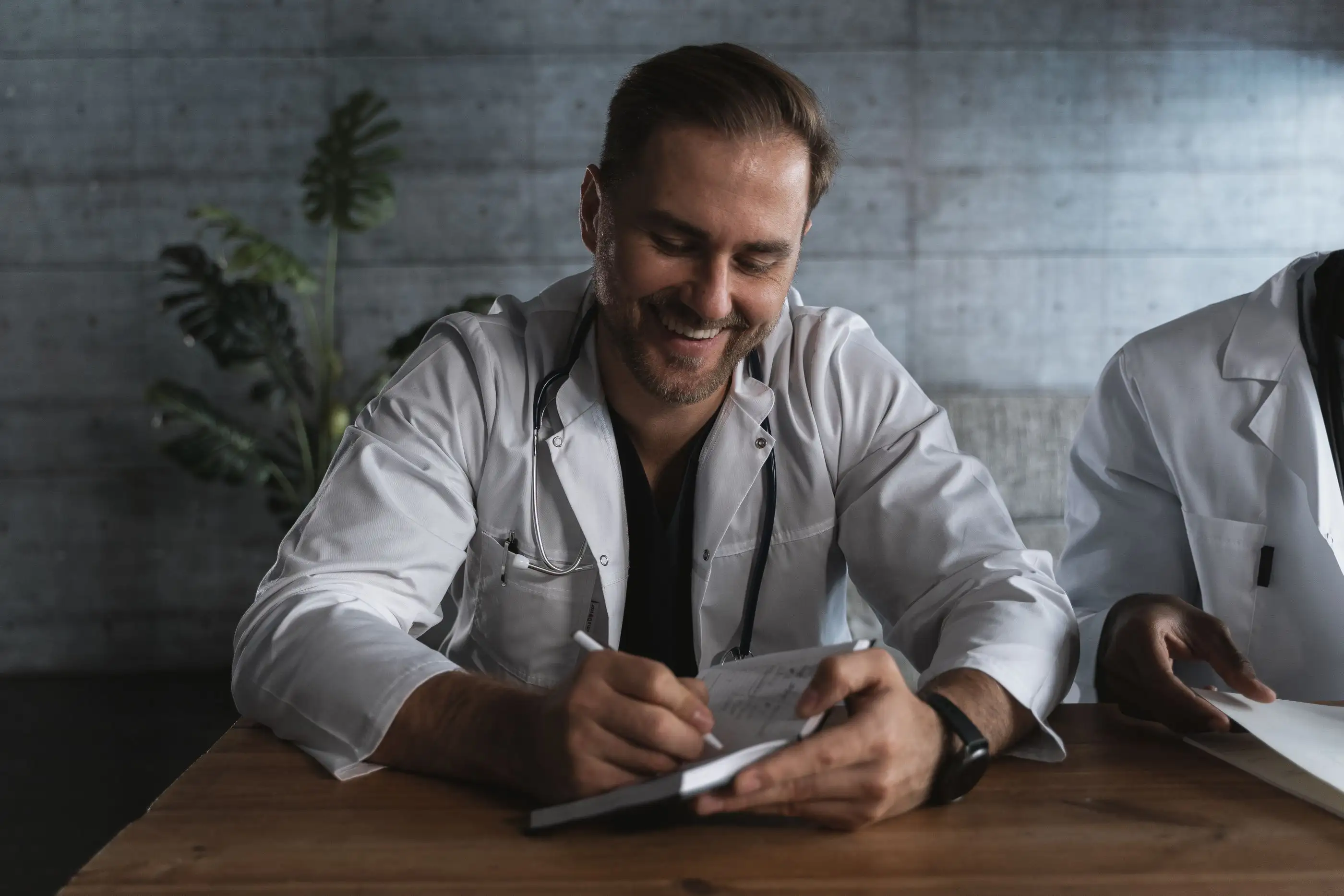 A smiling physician makes notes at a desk.