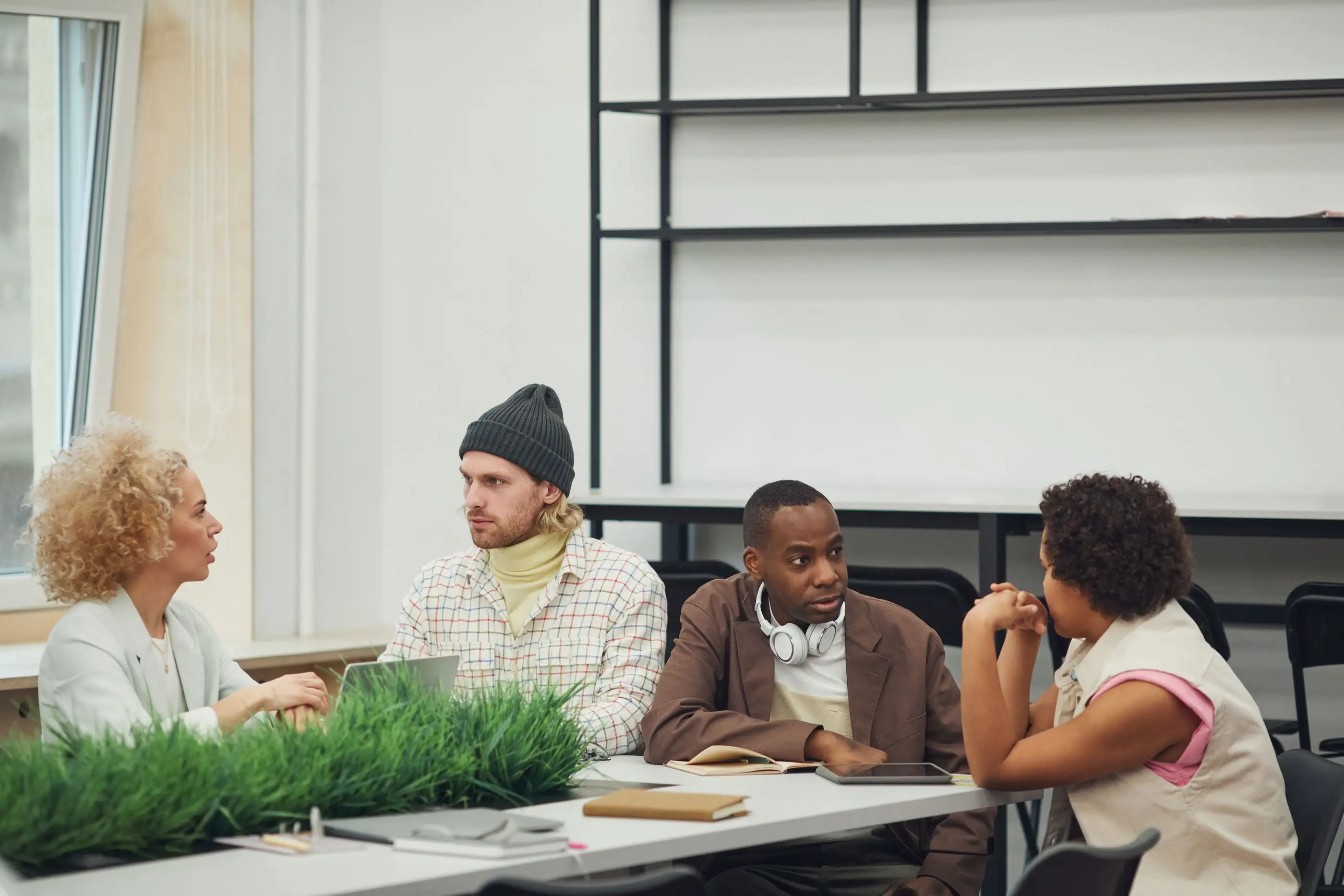 Four colleagues talk around a table in a bright meeting room.