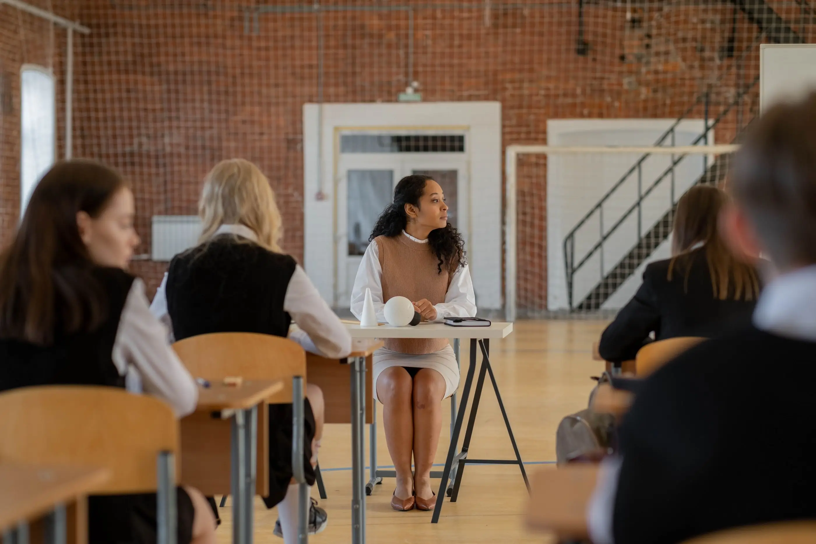 An instructor teaches a small class in a bright, brick-walled classroom.