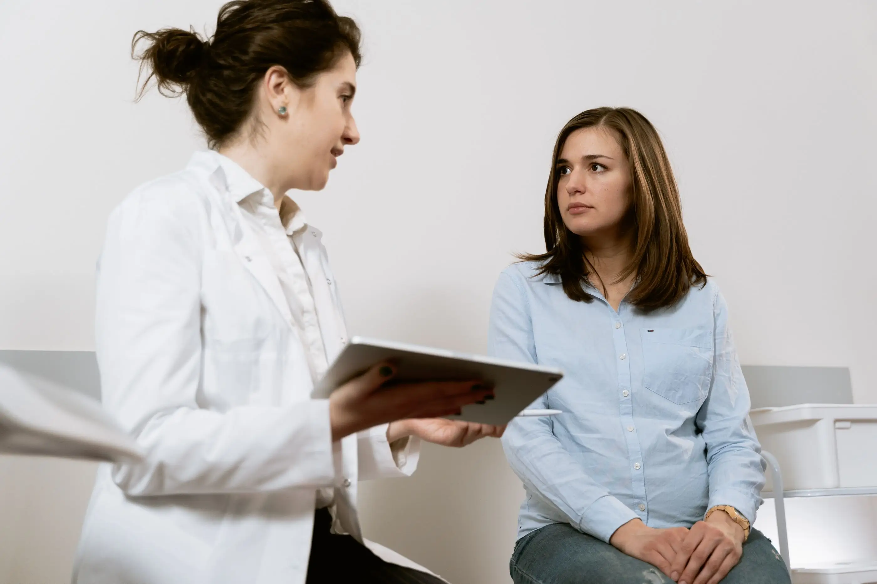 A pharmacist in a white coat talks a patient through information on a tablet.