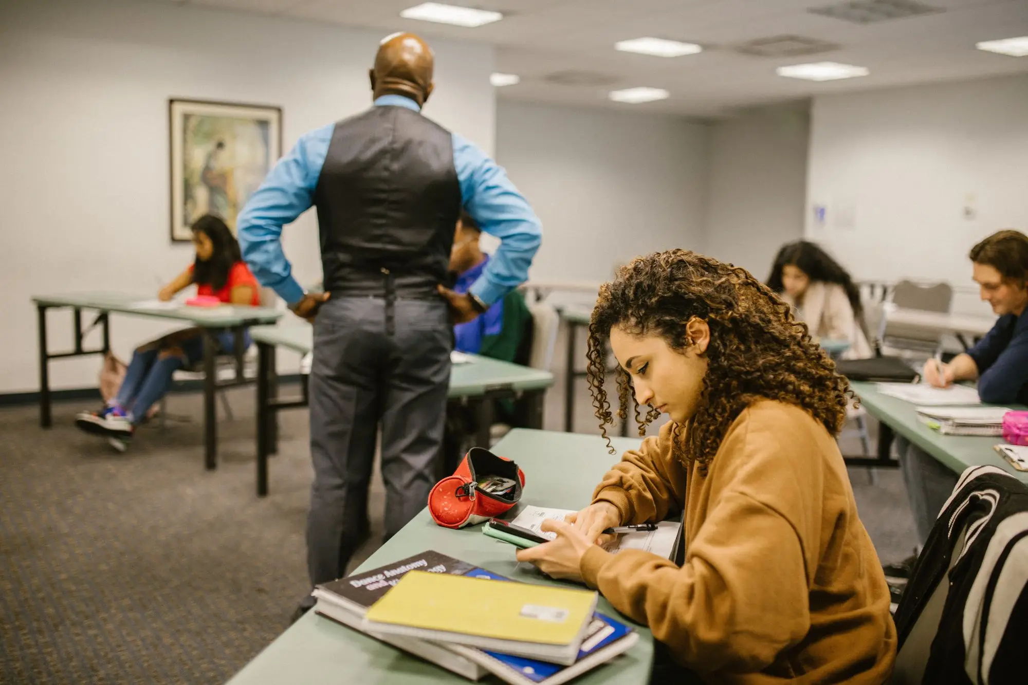 Students work at their desks while an instructor walks the classroom.
