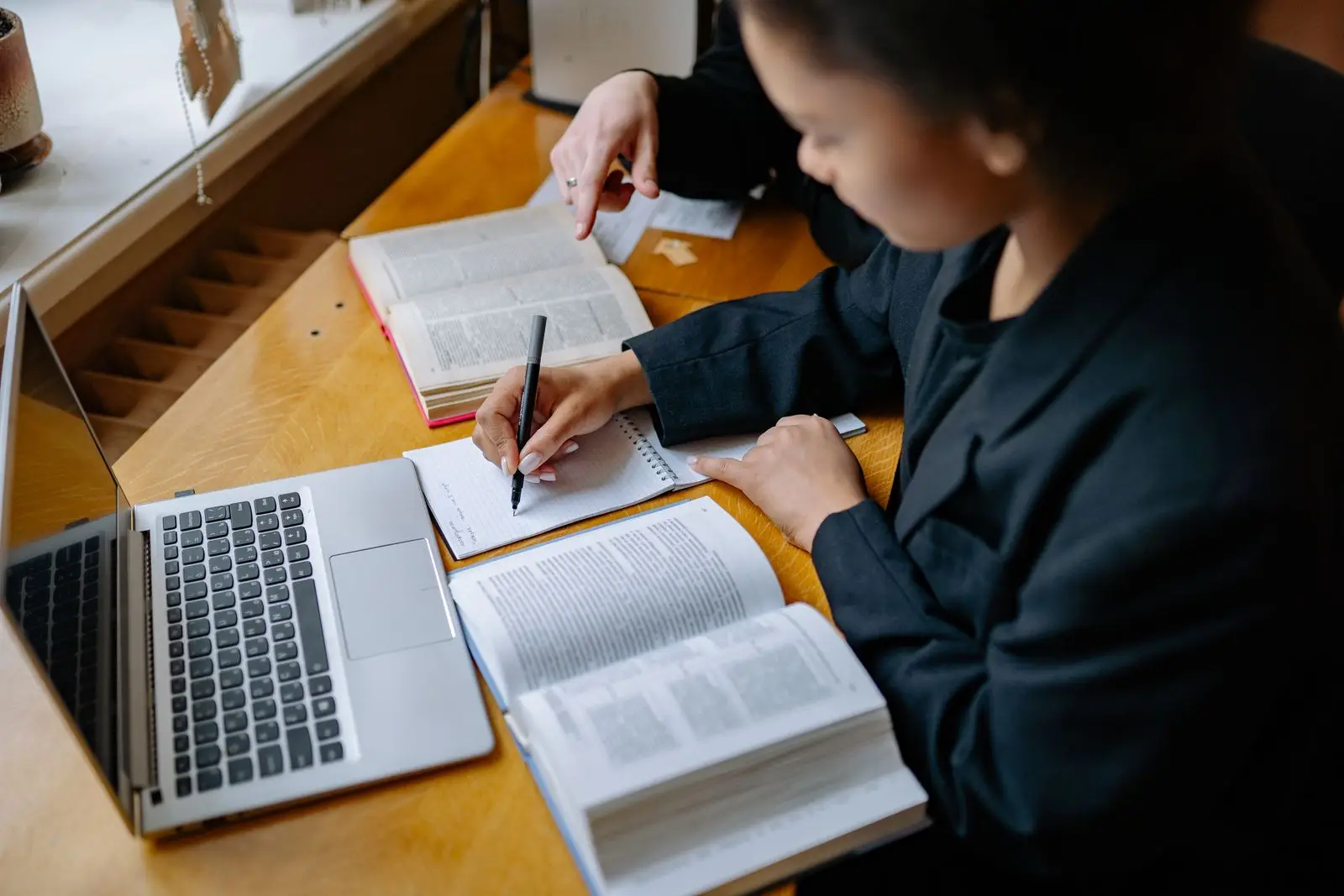 A reader takes handwritten notes from an open book beside a laptop.