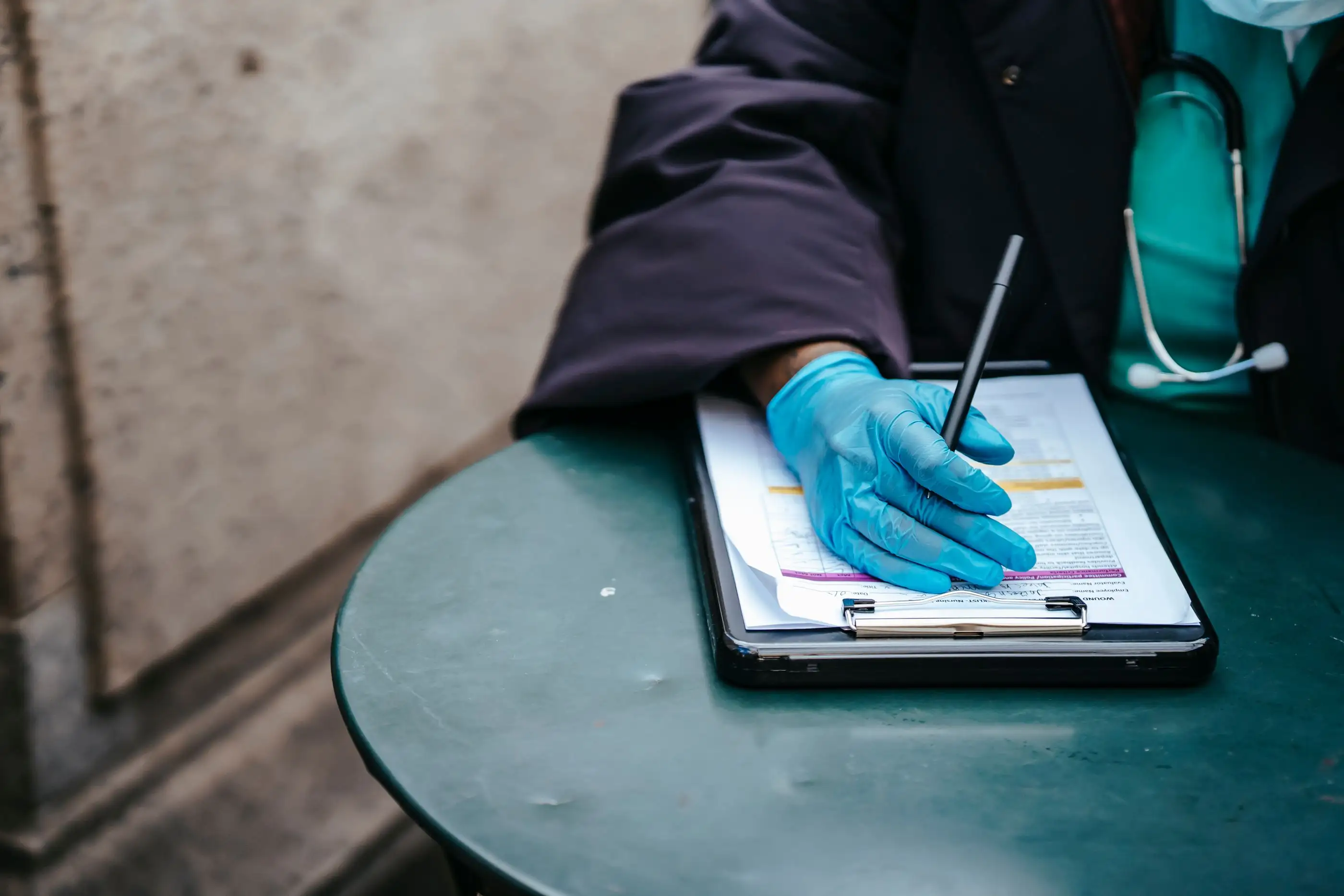 A gloved hand writes on a chart on a clipboard.