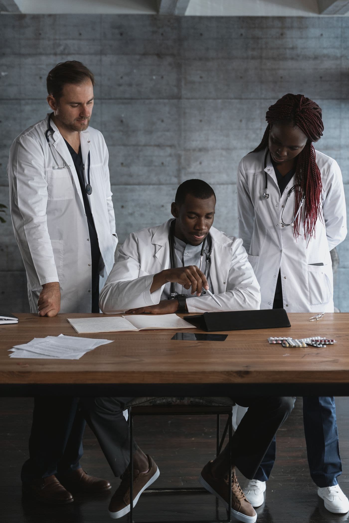 Three clinicians in white coats review papers together at a desk.